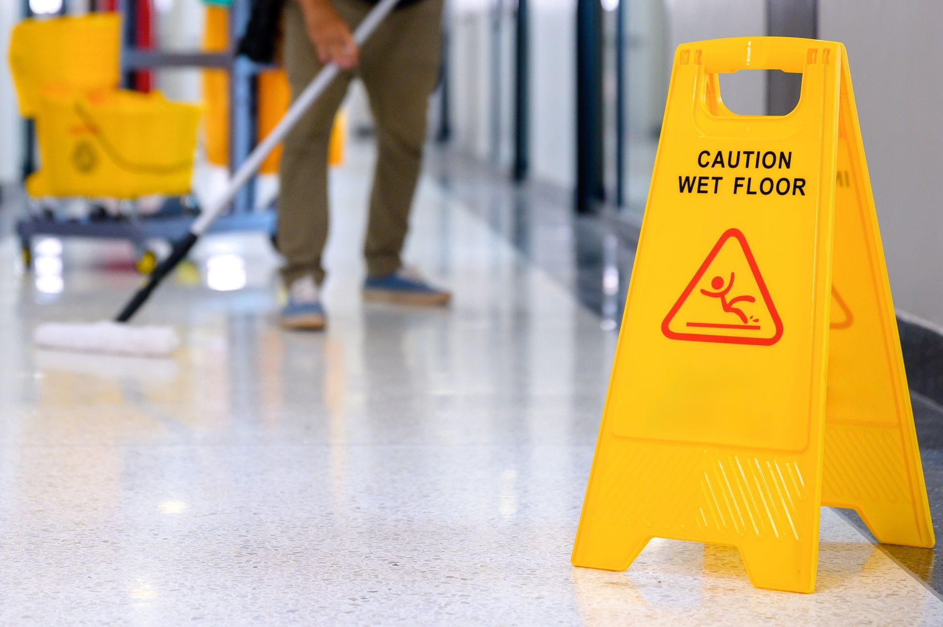 Janitor mopping a hallway behind a wet floor sign