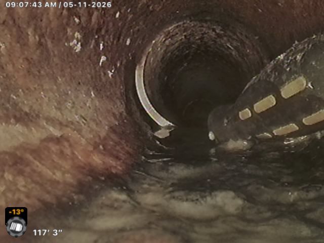 Inside a circular sewer pipe, murky water flows past a small illuminated section on the right.