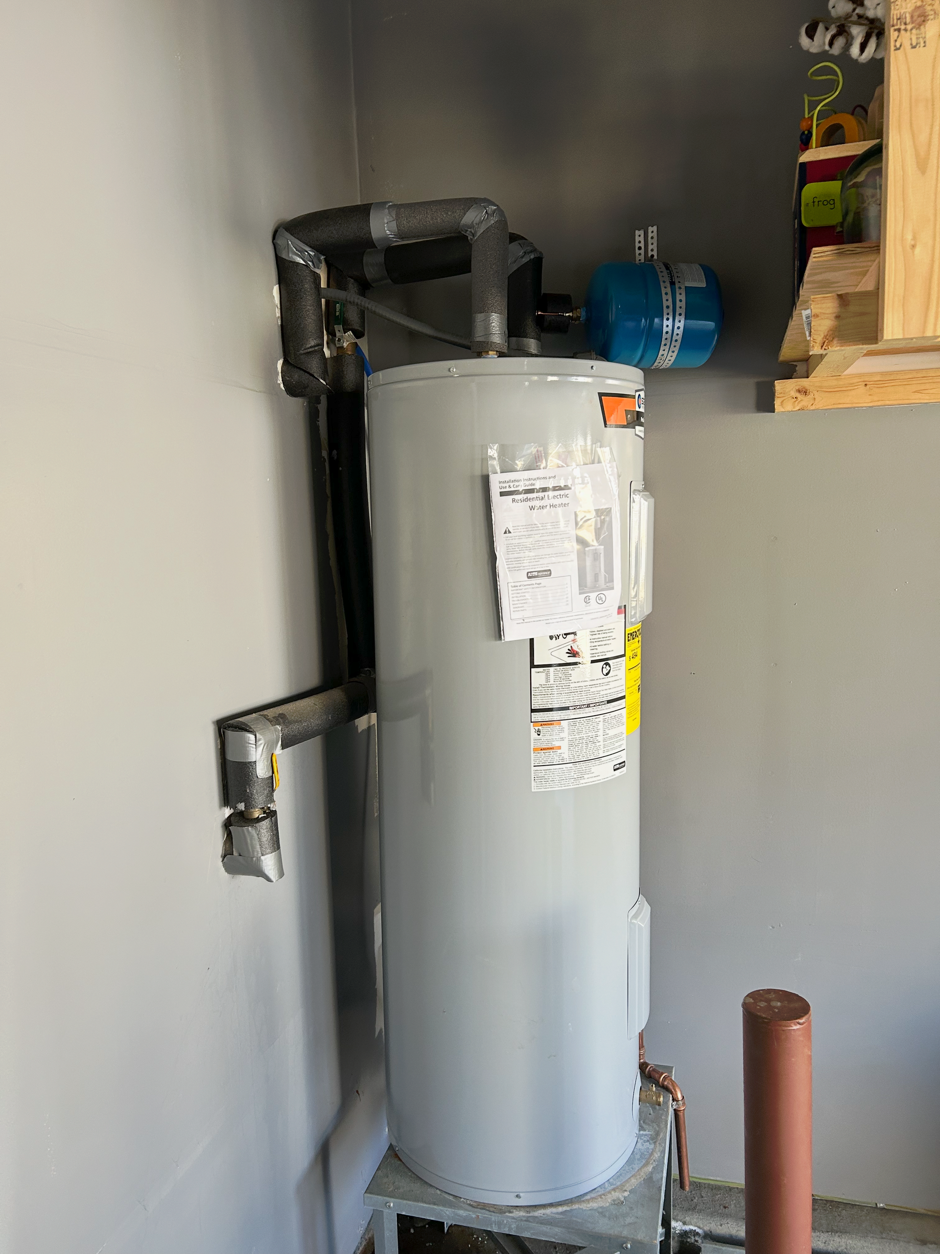 Water heater with pipes in a utility room against a gray wall.