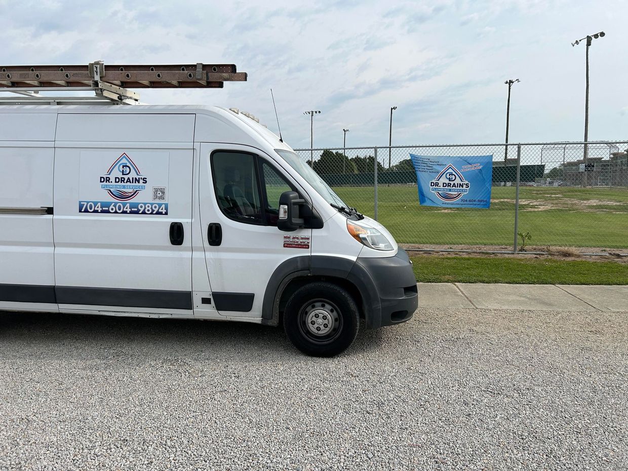 White service van parked on gravel beside a sports field, with a blue sign in the background