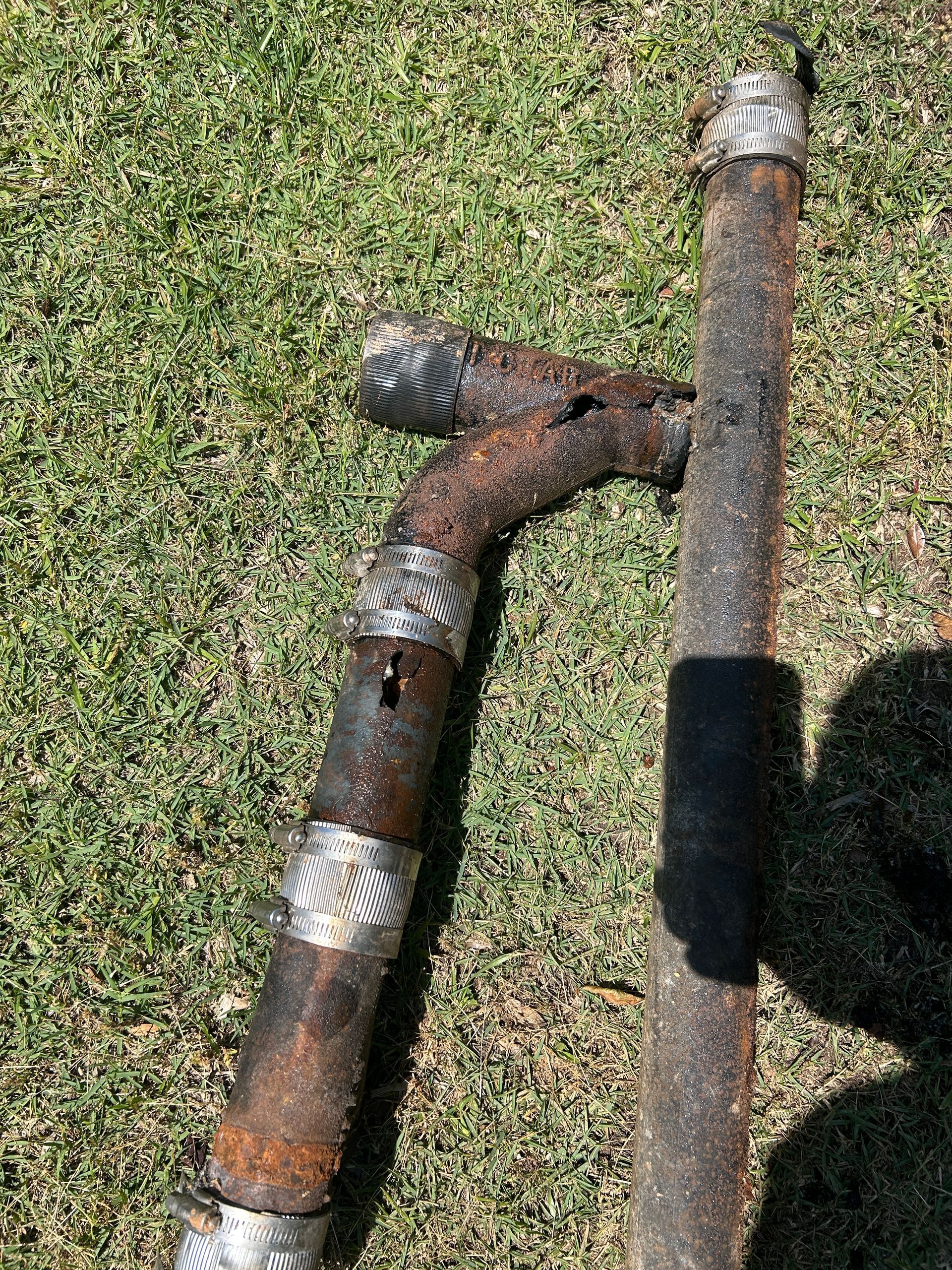 Two rusted metal pipes lying on grass, one bent with a curved joint.
