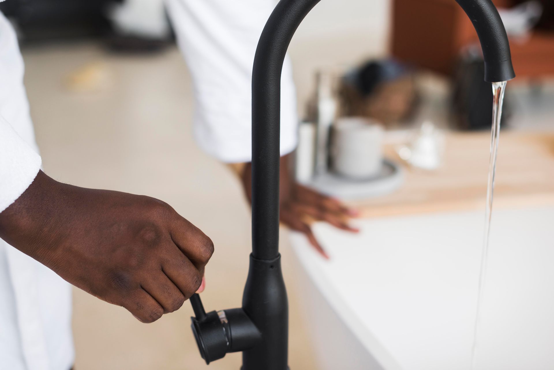 Person turning on a black kitchen faucet with running water at a sink