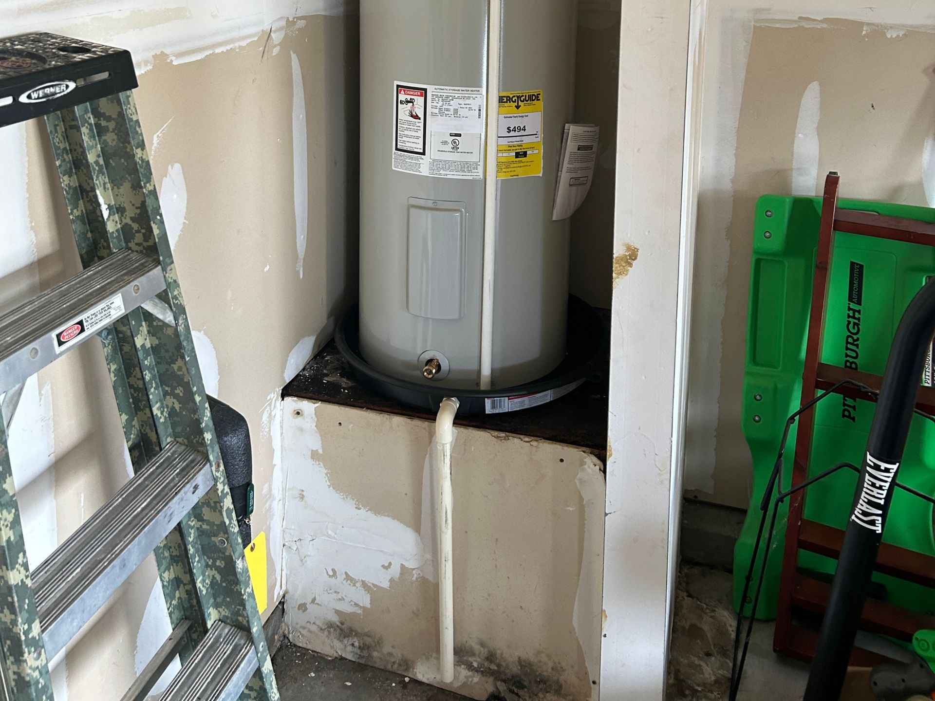 Water heater in a partially finished closet with exposed ducting and drywall patches