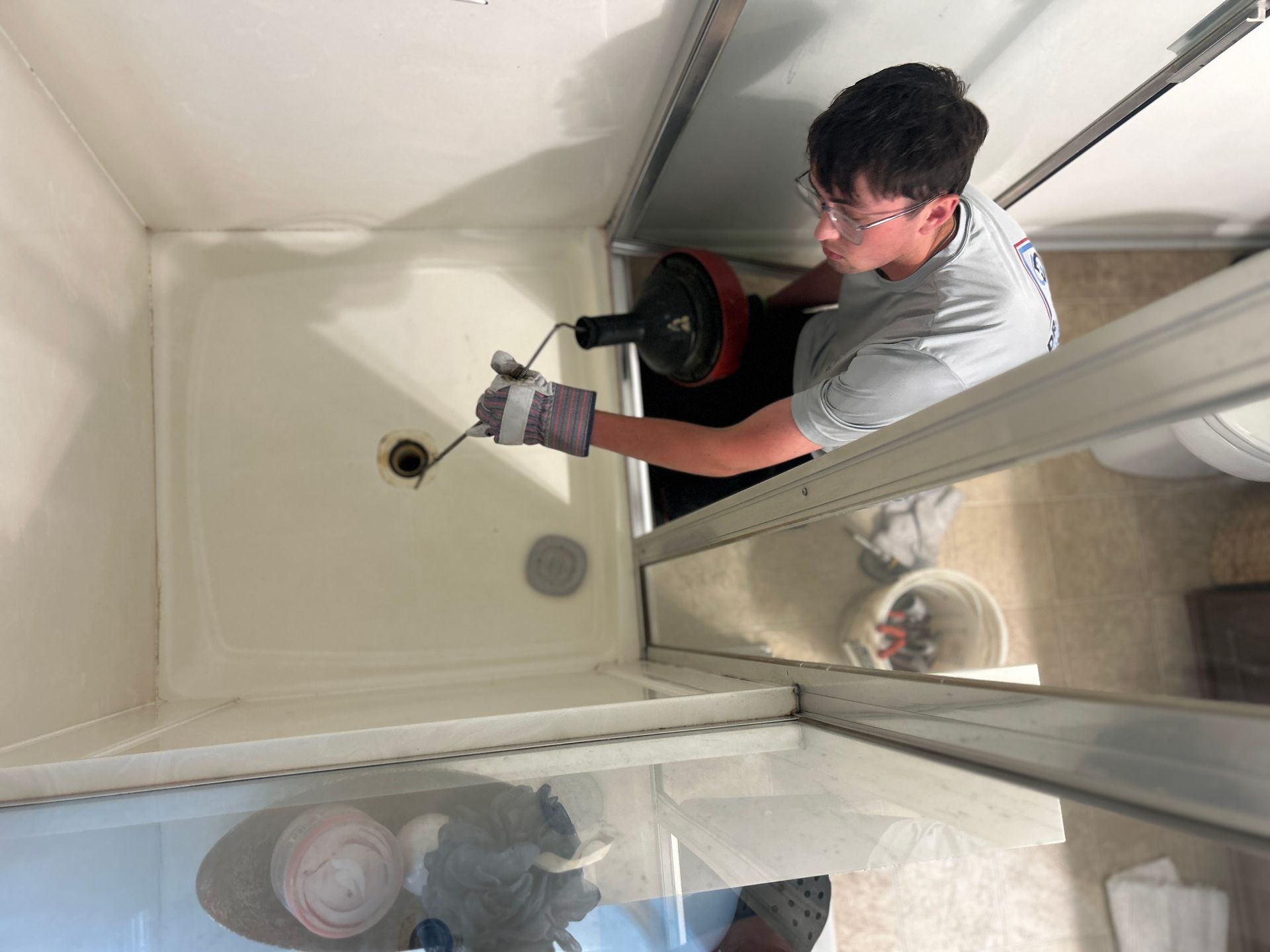 Worker using a drain-cleaning machine in a white sink or shower stall