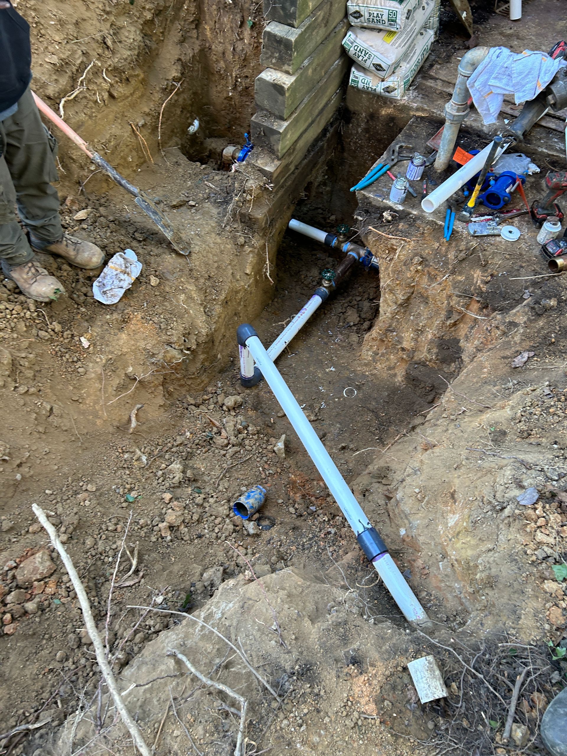 A man is digging a hole in the ground to install a pipe.