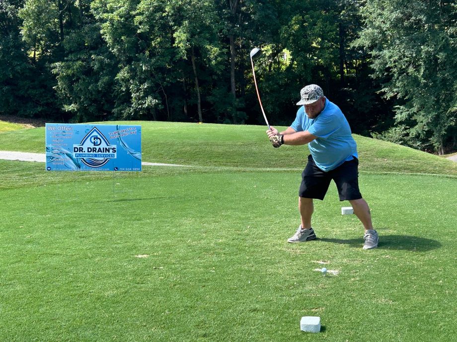 Golfer in blue shirt preparing to swing on a grassy course near a sign and wooded background