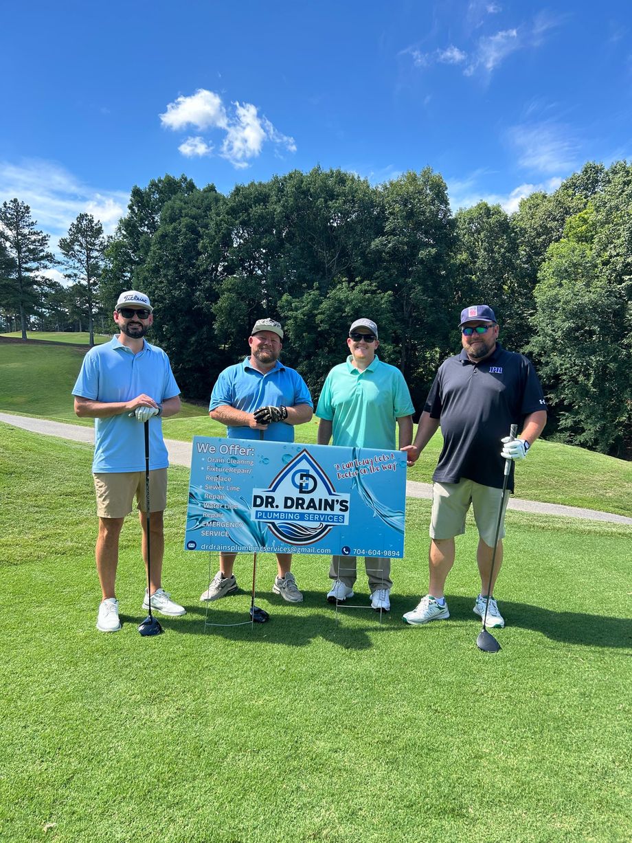 Four people standing on a golf course holding a blue banner under a sunny sky