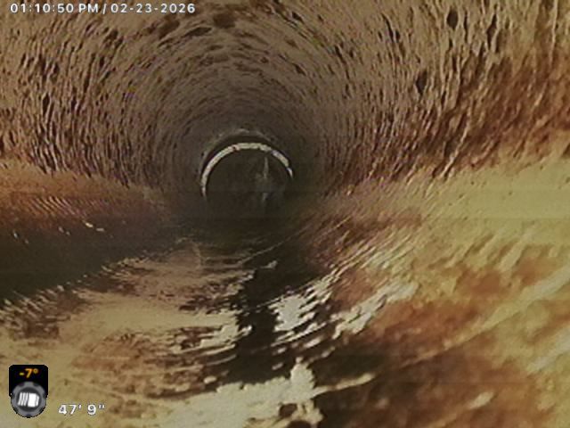 Inside a brick sewer pipe with flowing water and a dark circular tunnel ahead.