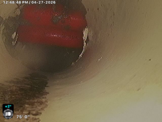 Inside a beige pipe, a red object blocks the opening, with dark buildup along the lower left edge.