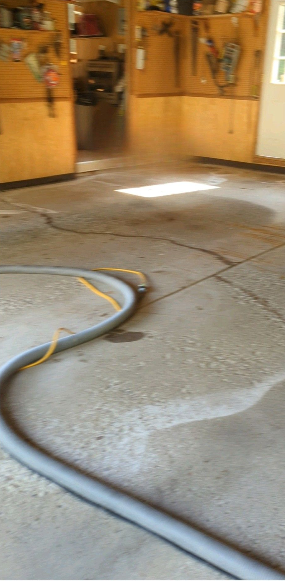 Garages or workshop floor with a hose or cable coiled across cracked concrete, sunlight near the back wall