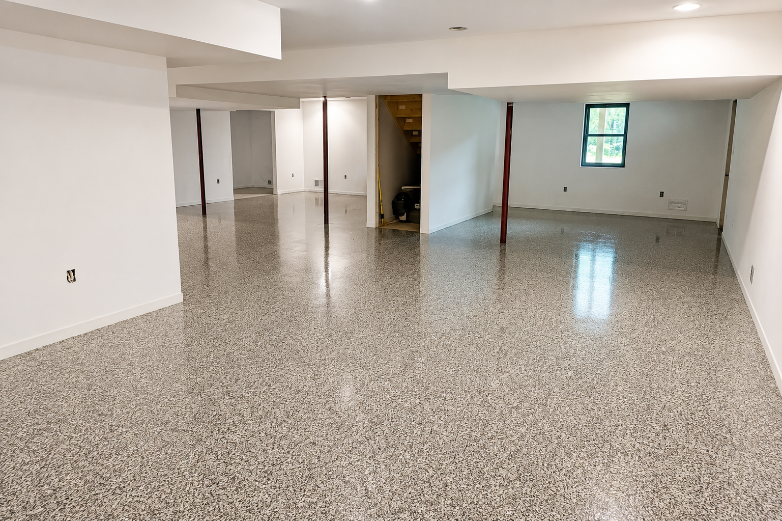 Empty basement room with speckled floor, white walls, and small window.