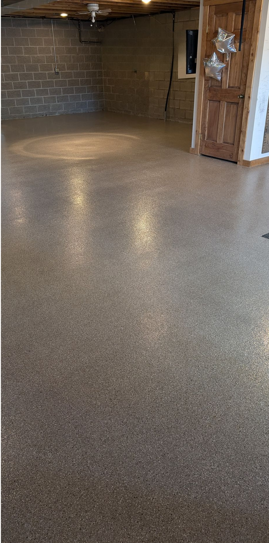 Empty basement with speckled epoxy floor and cinder block walls, lit by a bright floor spotlight.