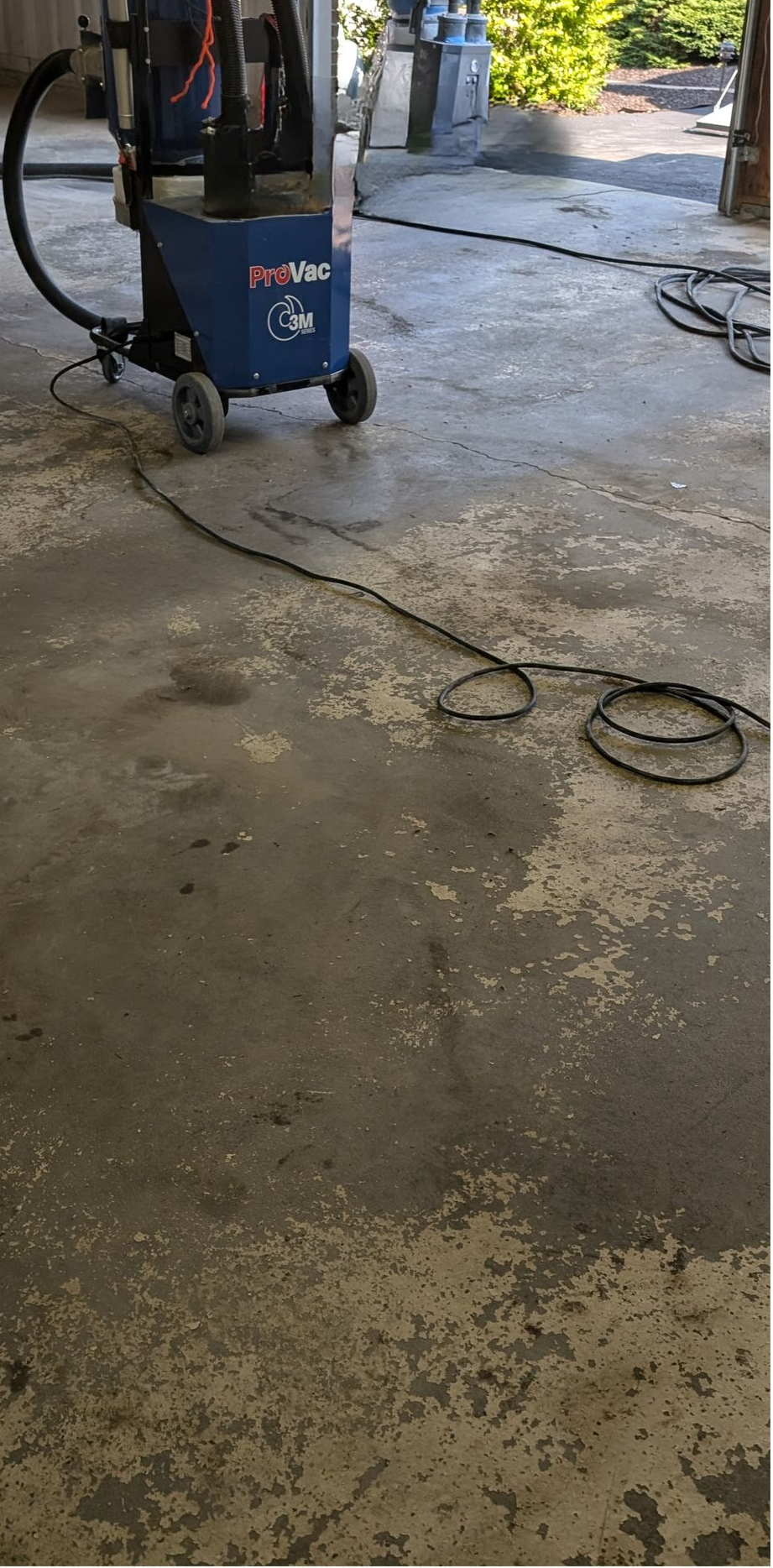 Blue industrial floor machine on a wet concrete garage floor with hoses and cords nearby