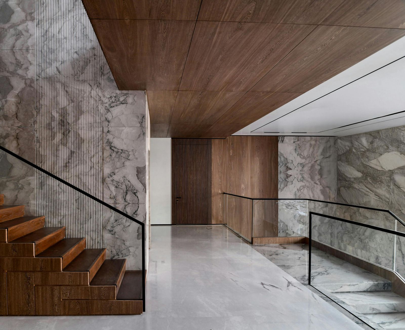 Modern interior staircase with wood steps, marble walls, glass railing, and polished white floor