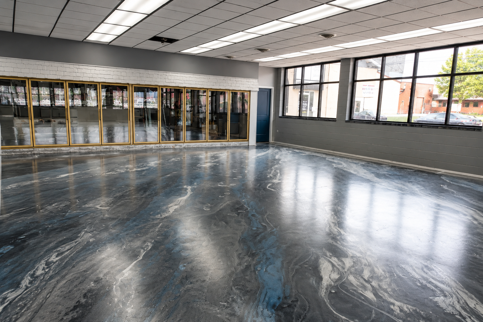 Empty lobby with glossy concrete floor, glass doors, and large windows letting in daylight.