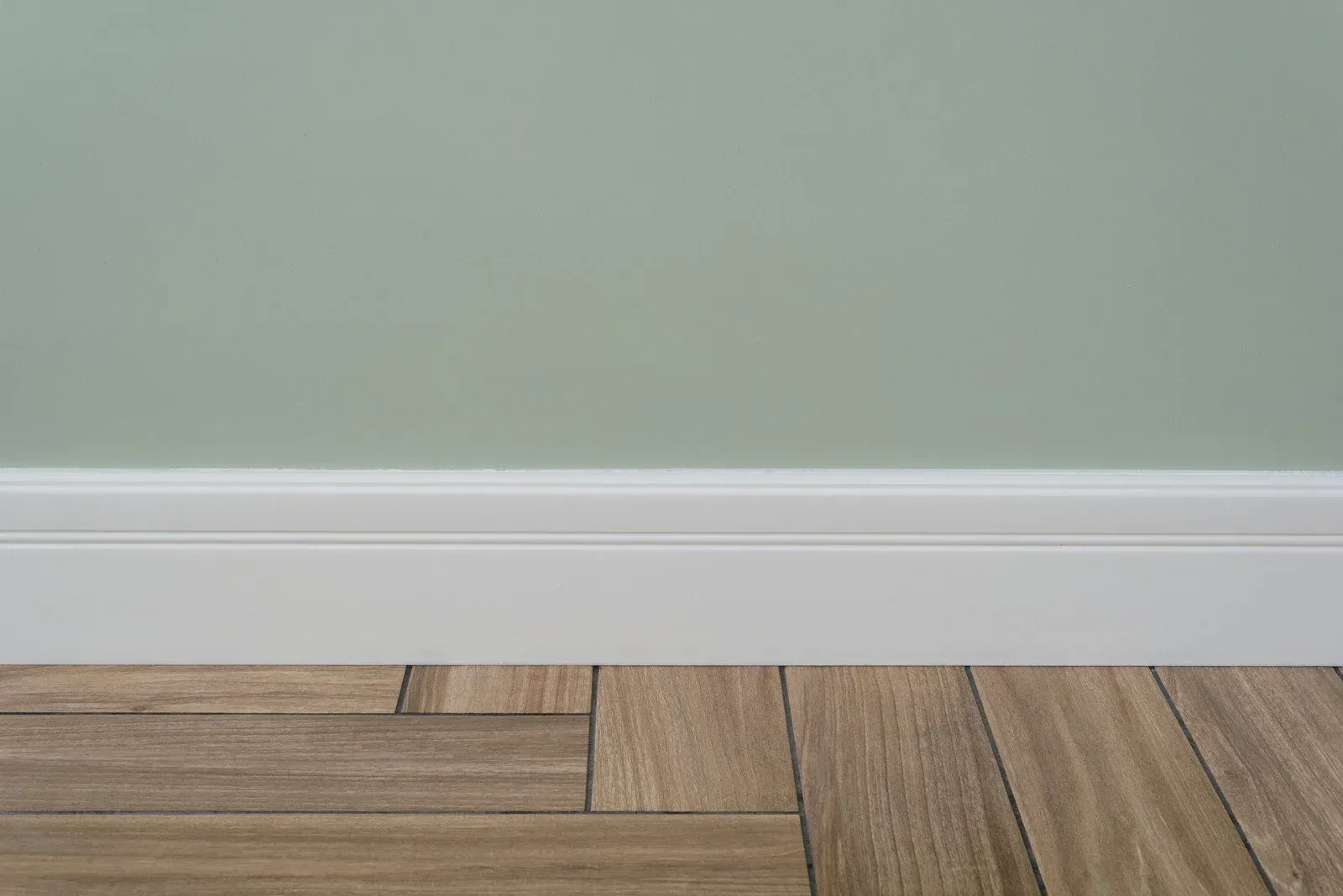 White baseboard against pale green wall above wood-patterned floor.