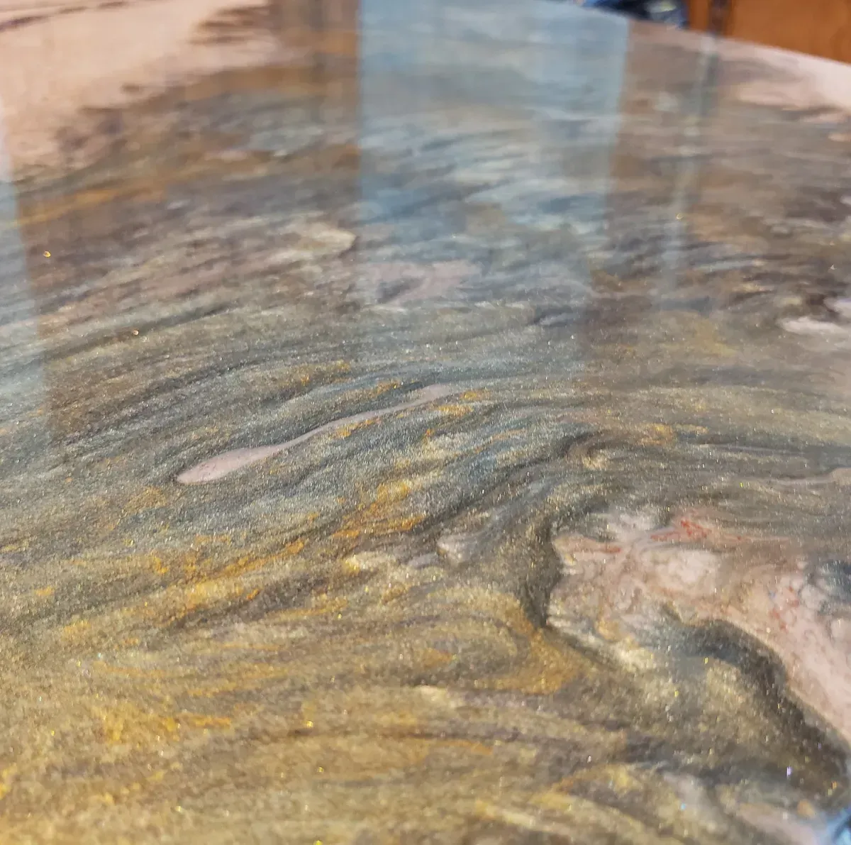 Close-up of a glossy wood-grain surface with swirling brown, gray, and gold tones