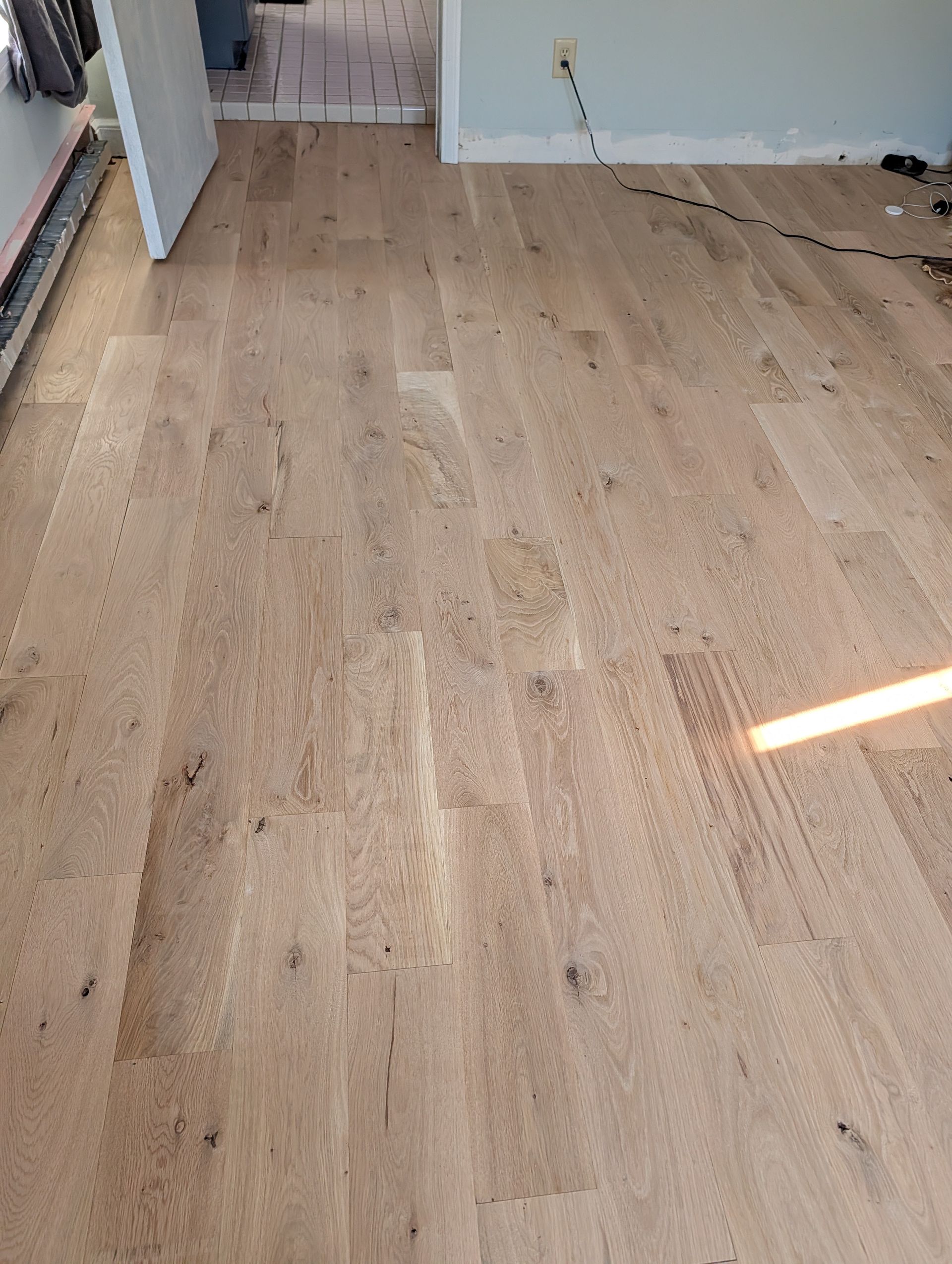 Empty room with light wood flooring, a white wall, and a striped patch of sunlight near the bottom right.