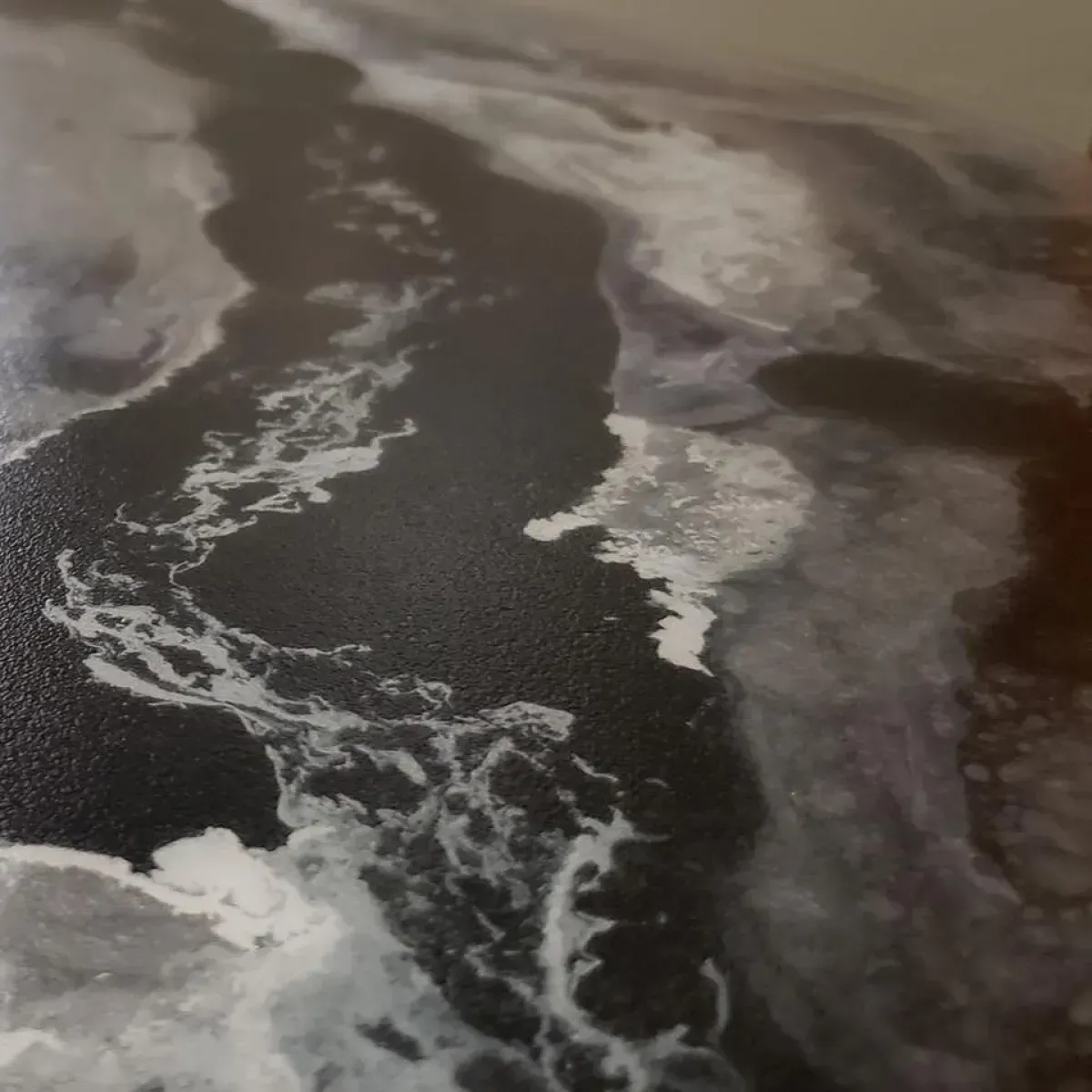 Aerial view of foamy waves washing over a dark shoreline or volcanic beach