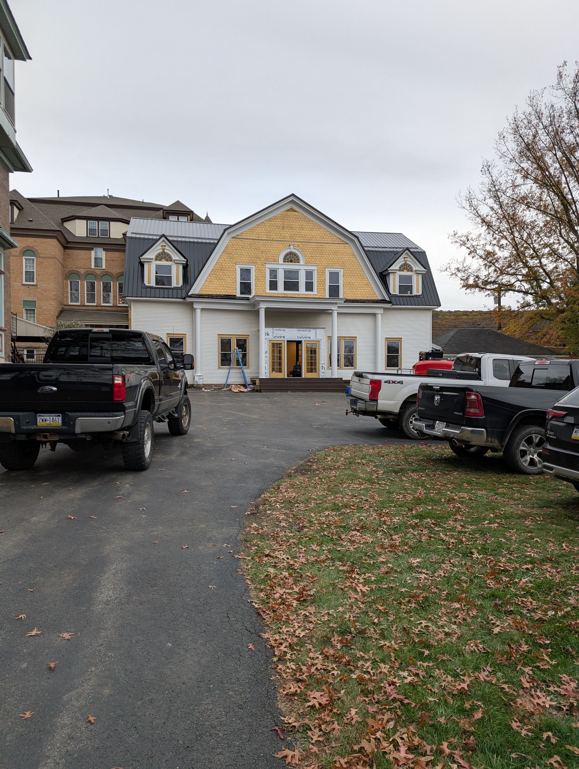 Yellow house with white trim, parked trucks, and a driveway covered in fallen leaves