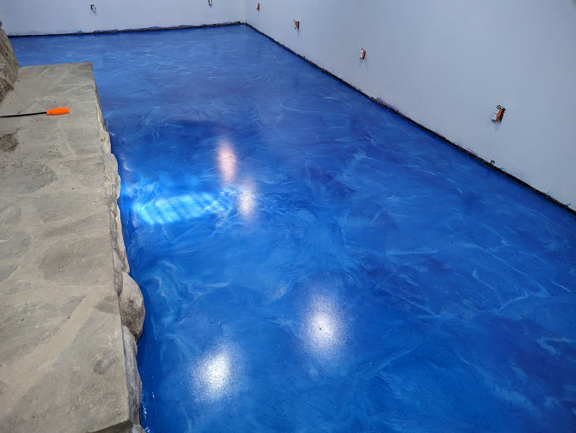 Blue epoxy-coated floor in an empty room with white walls and bright reflections