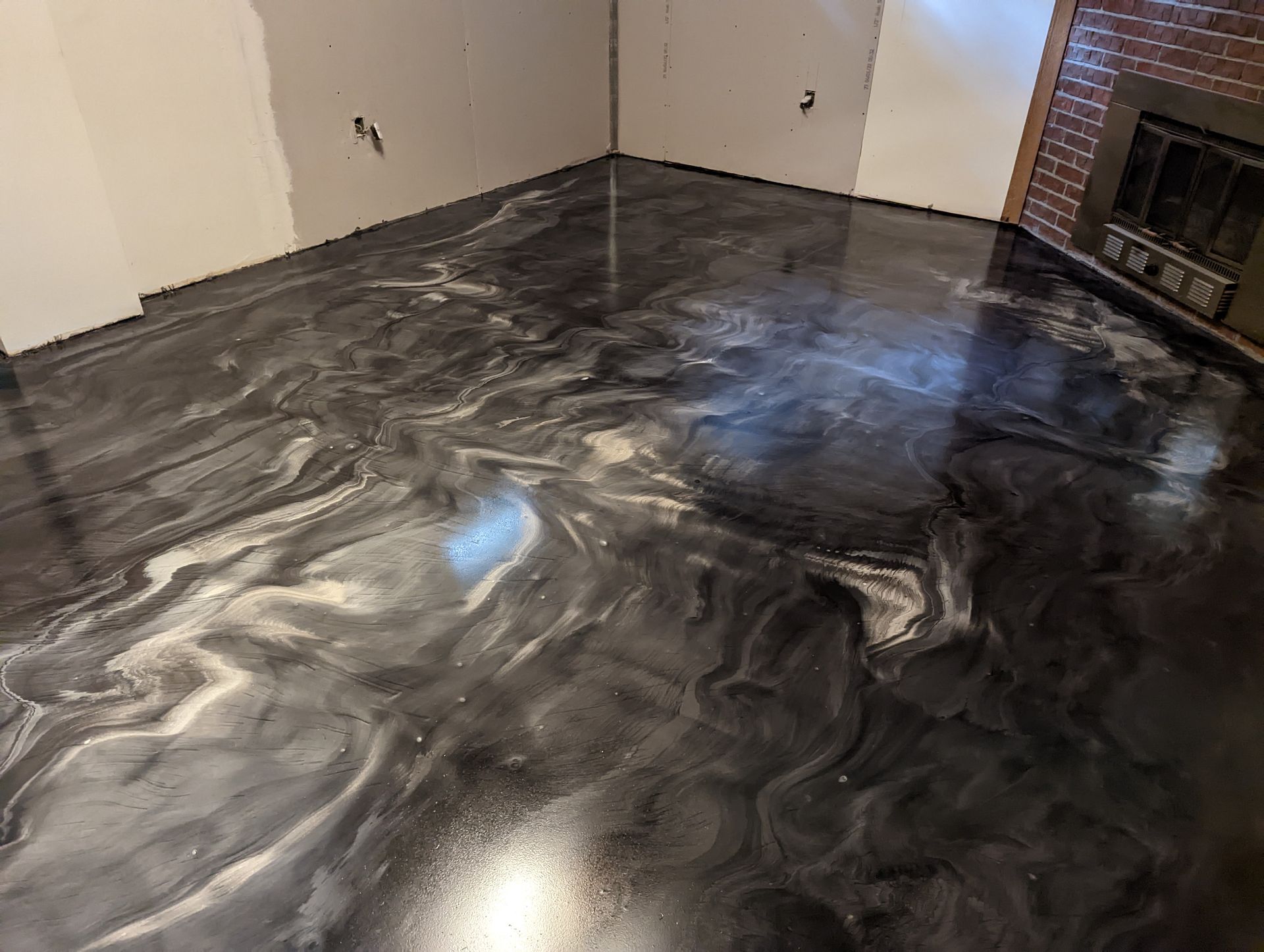 Shiny black swirled epoxy floor in an empty room with a fireplace on the right