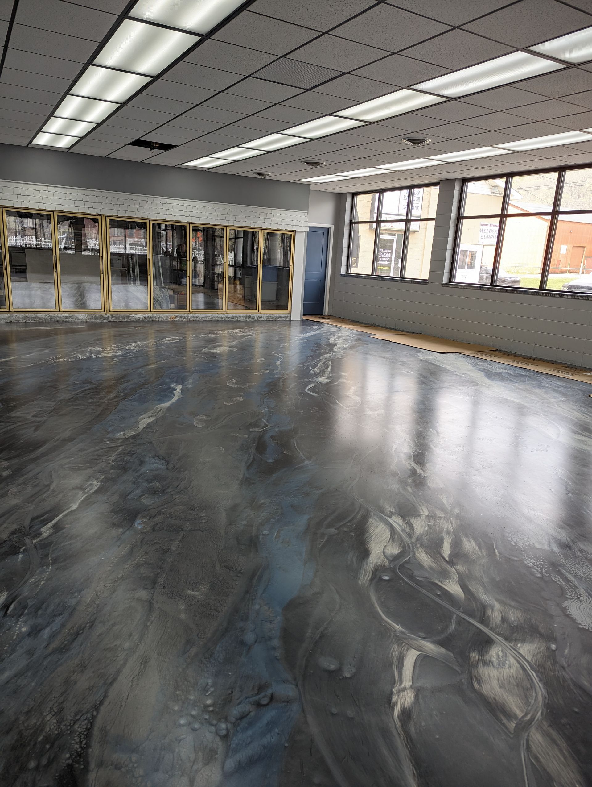 Empty dance studio with mirrored wall, fluorescent ceiling lights, and a glossy black floor.