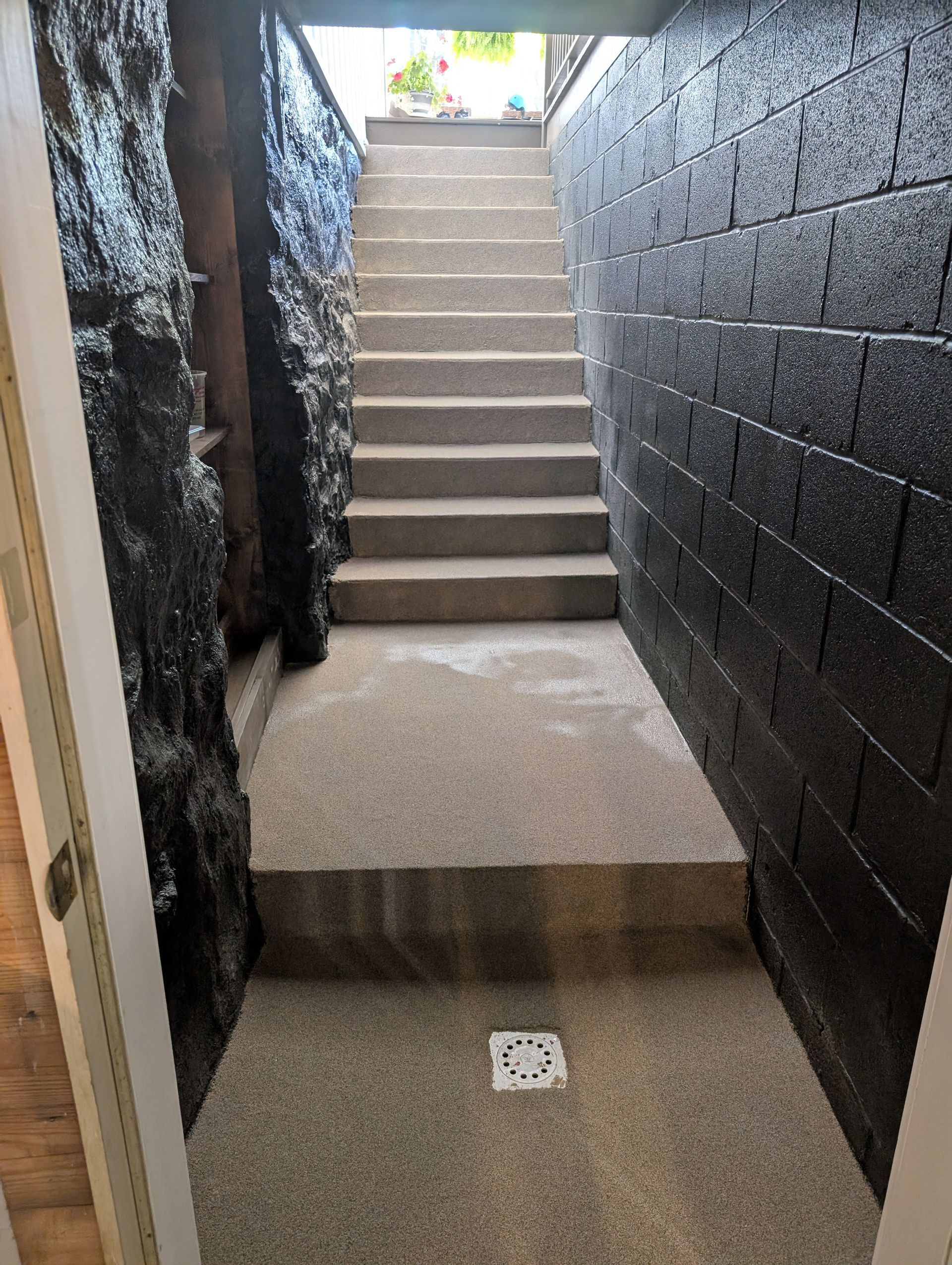 Narrow concrete stairwell with black walls leading up to bright daylight