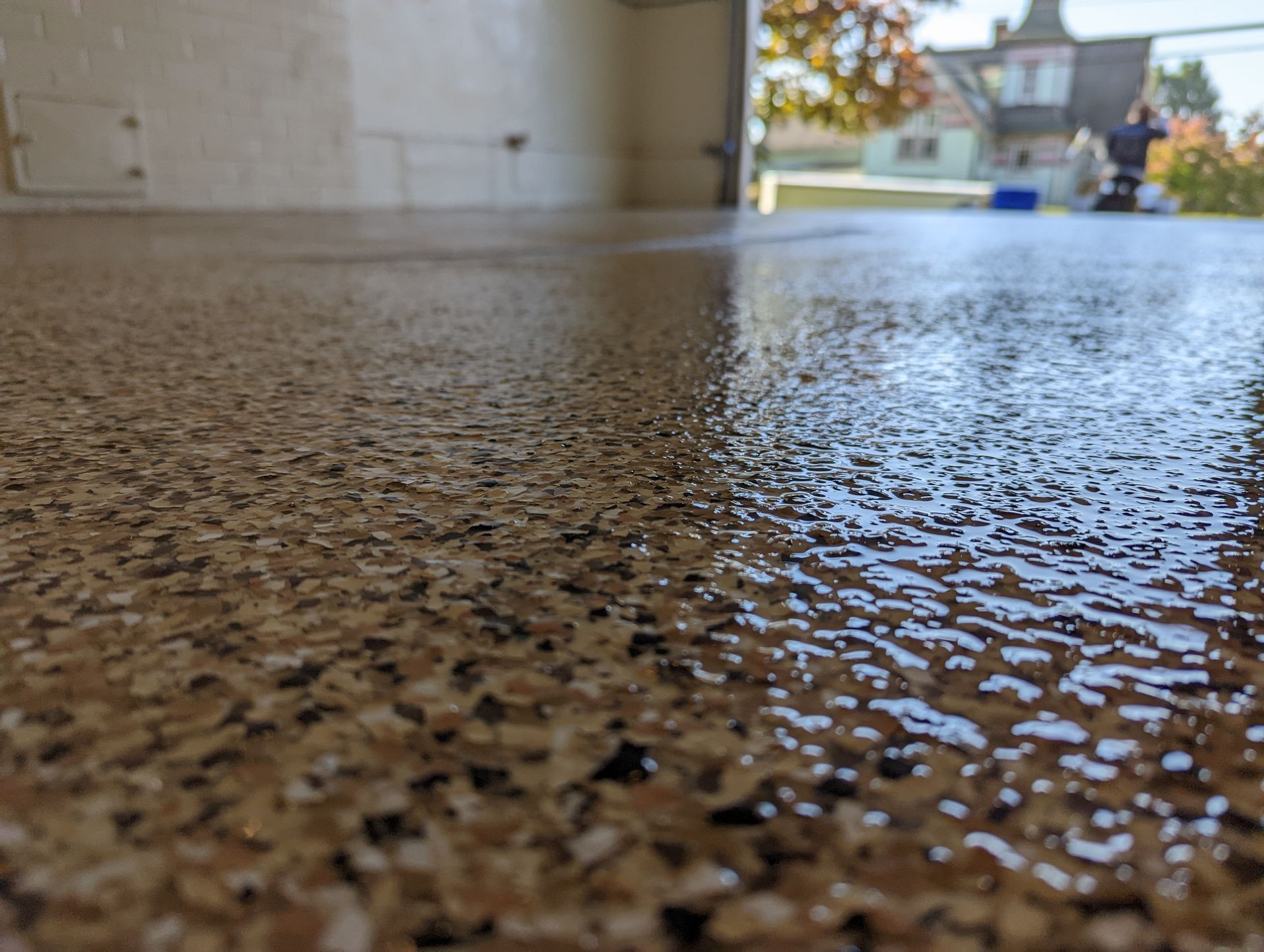 Close-up of wet speckled concrete floor with a blurred house and autumn trees in the background