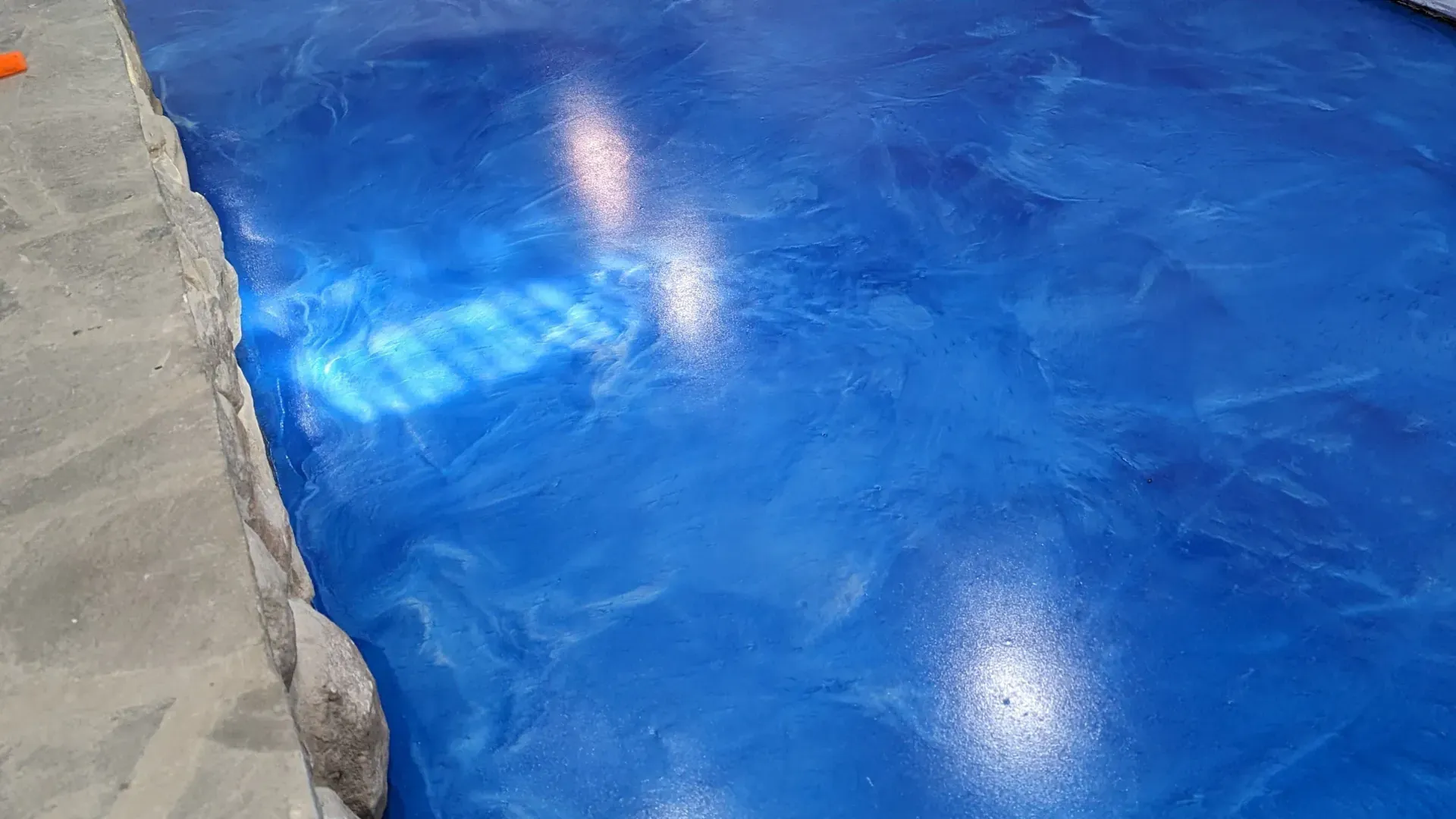 Blue painted floor beside a rough concrete edge, with light reflections on the glossy surface.