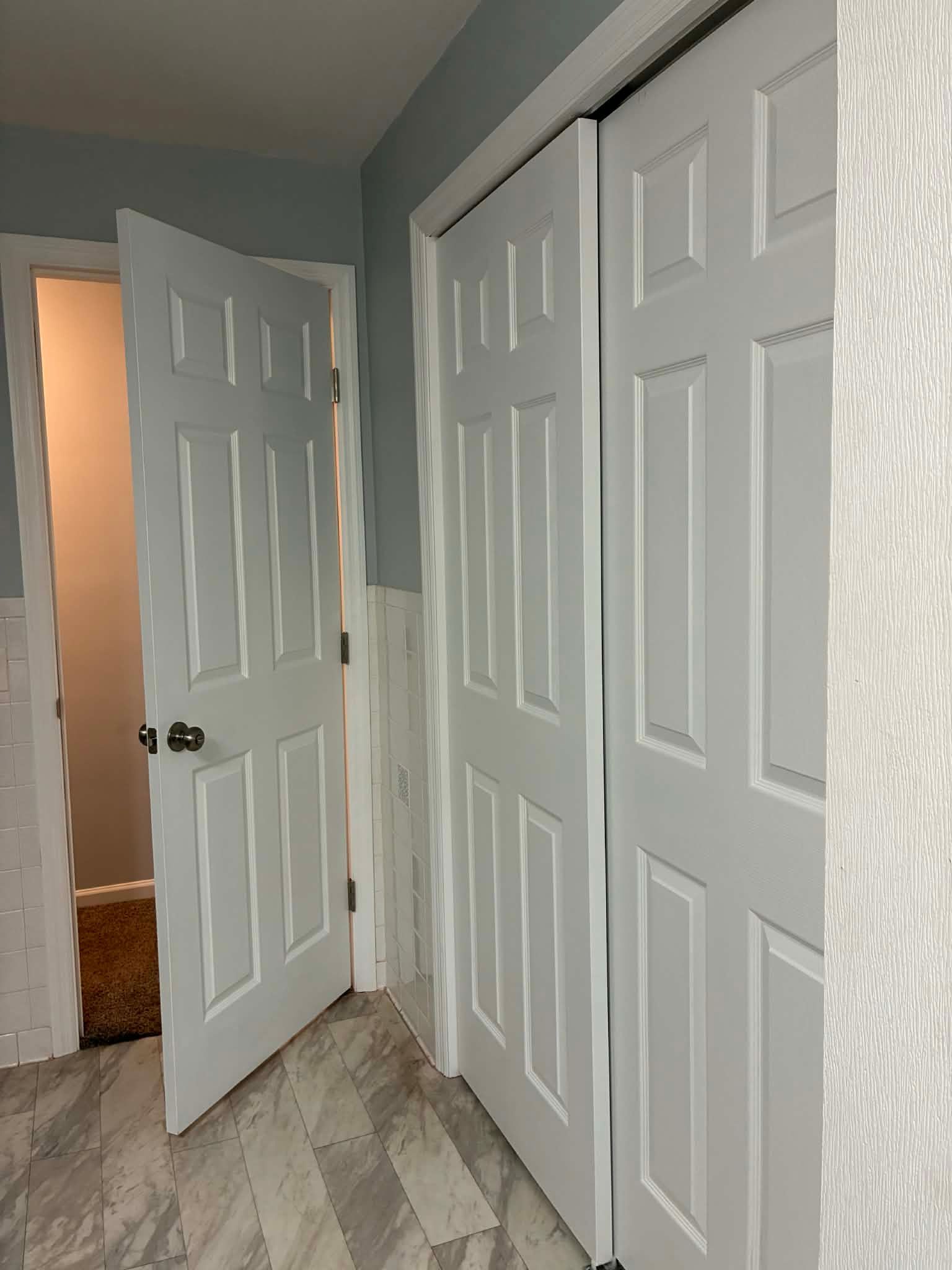 Hallway with white closet doors, a partially open white door, and gray walls with wood-look flooring