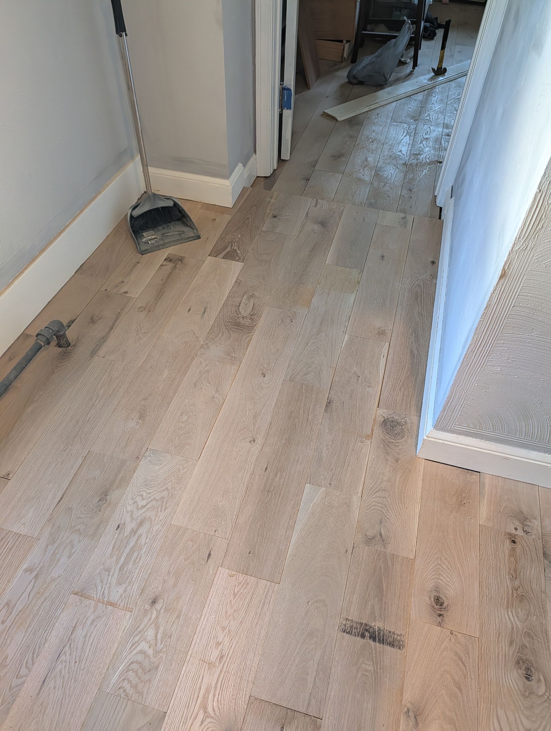 Hallway with damaged wood floor, debris, and a bucket near the wall