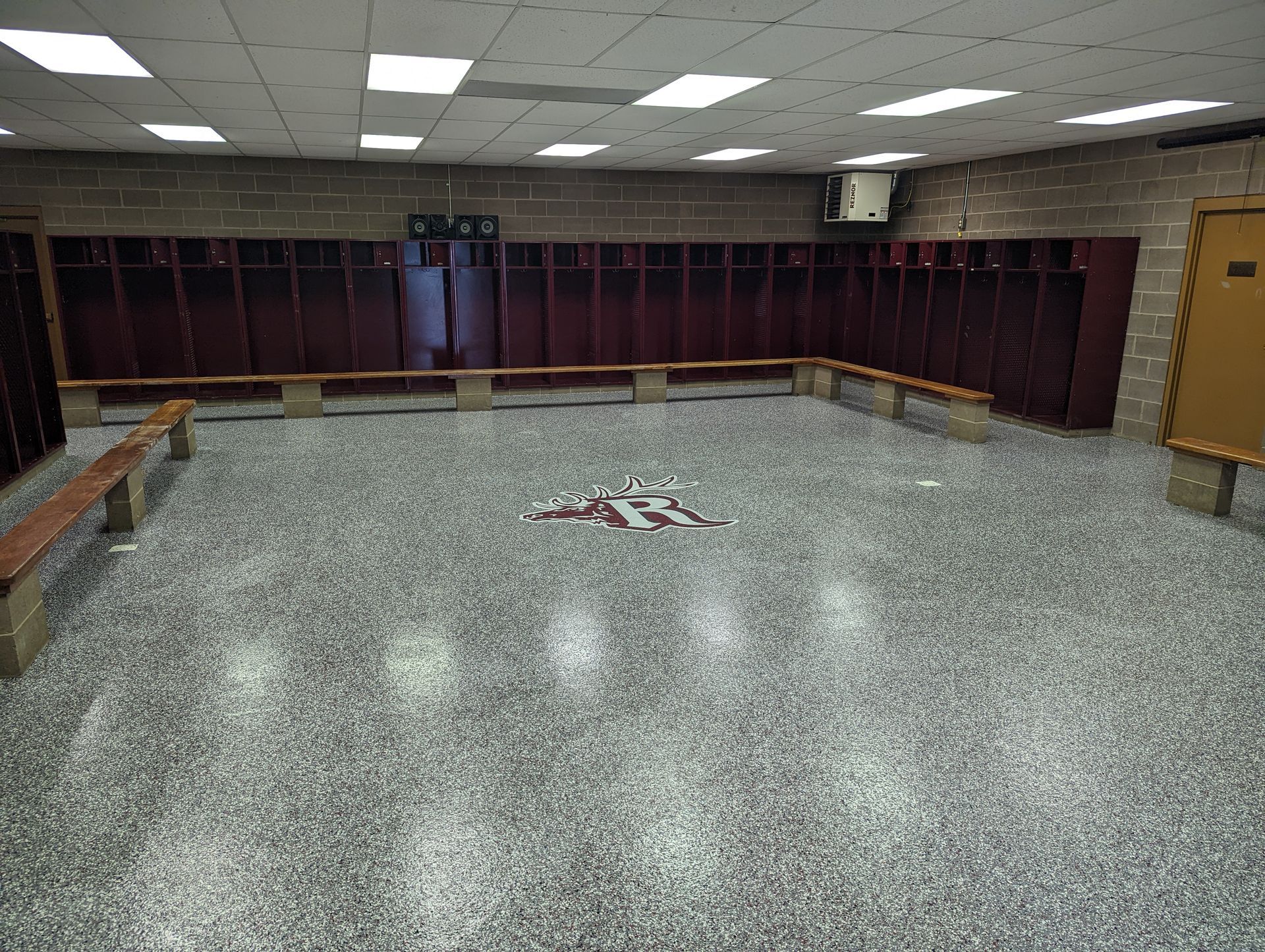 Empty locker room with maroon lockers, gray speckled floor, and fluorescent ceiling lights.