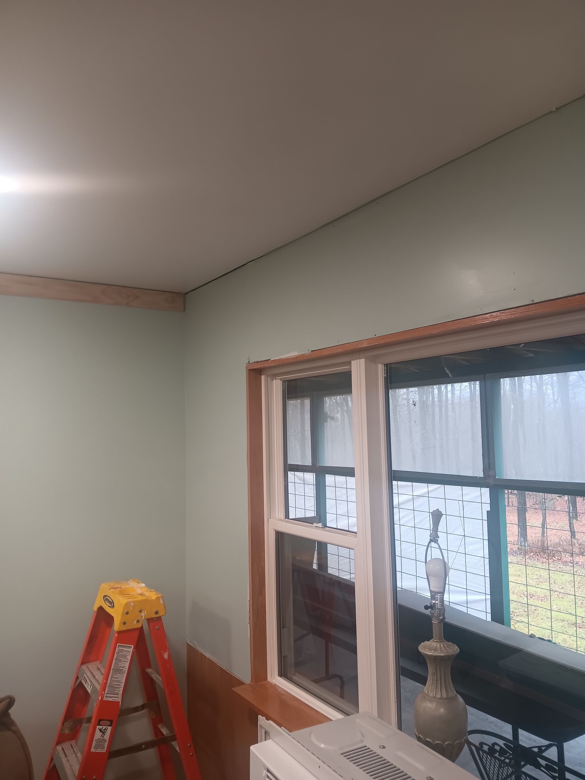 Interior room with green walls, a red ladder, and a large window under construction trim