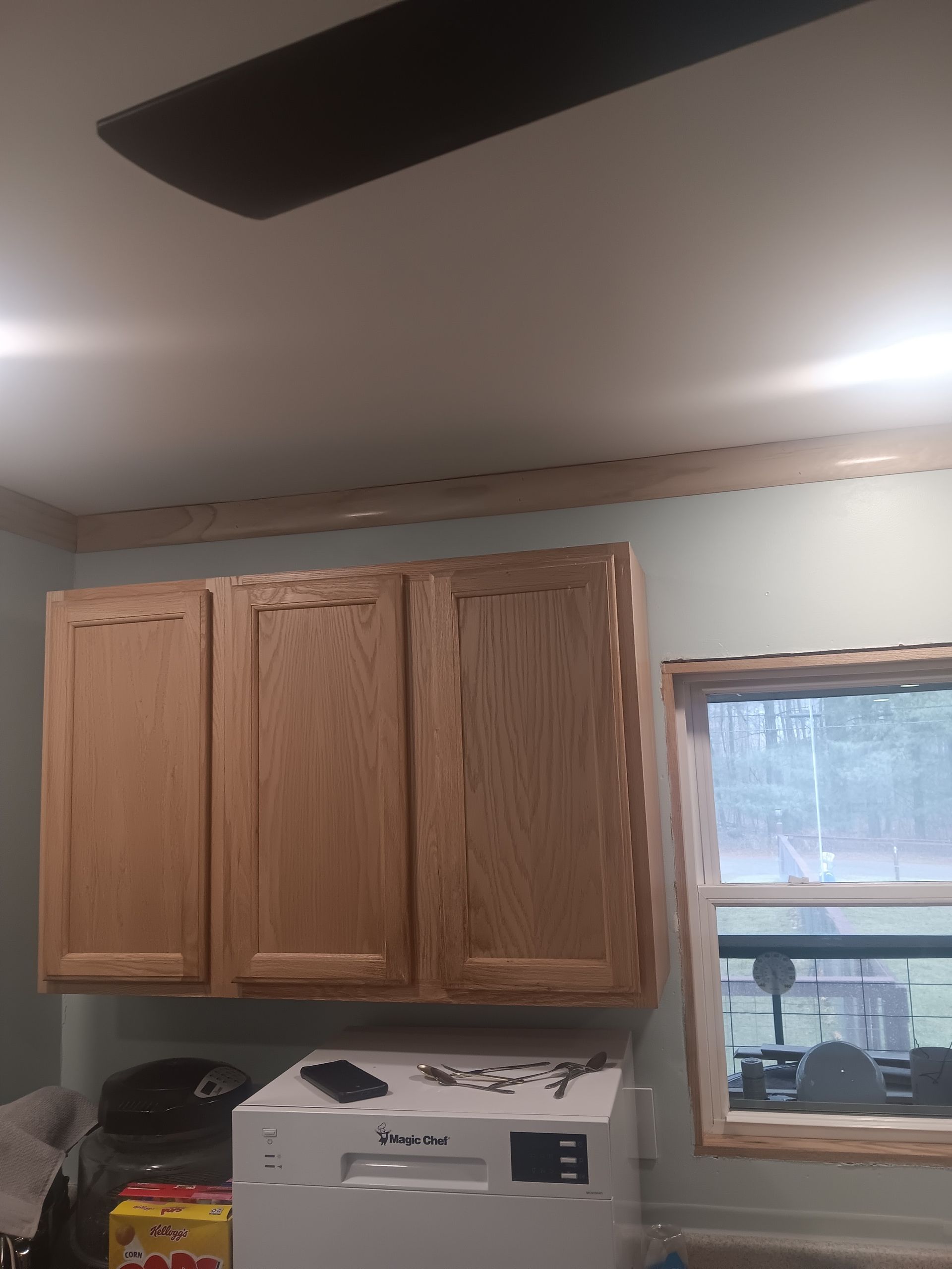 Kitchen wall with wooden cabinets, a printer on the counter, and a window beside them.
