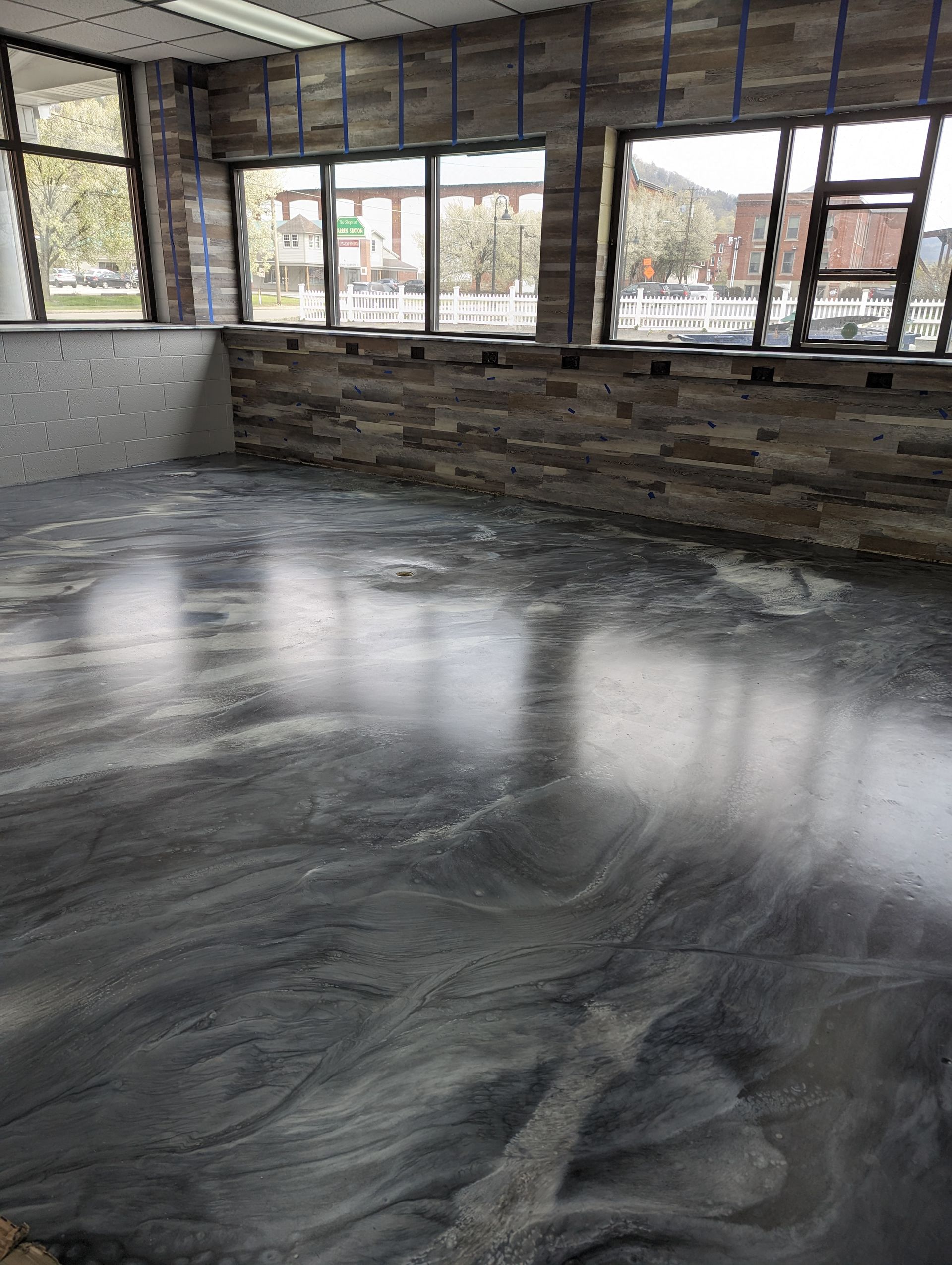 Empty room with polished gray floor, brick walls, and large windows letting in daylight.