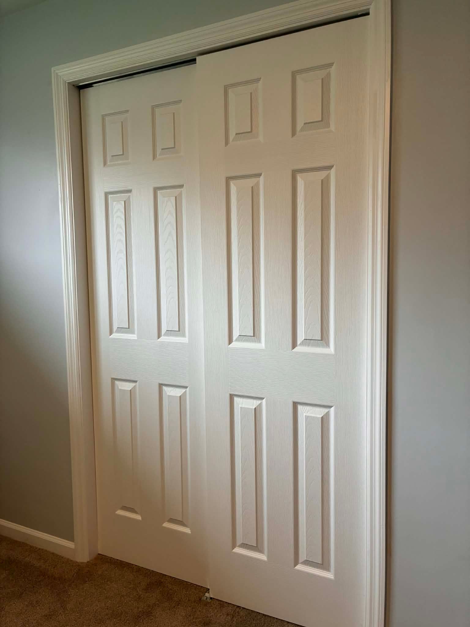 White bi-fold closet doors in a carpeted room against gray walls.
