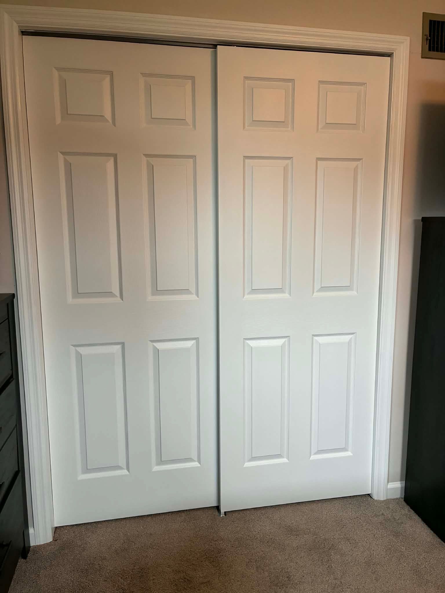 White double closet doors with raised panels in a beige room, viewed from the carpeted floor.