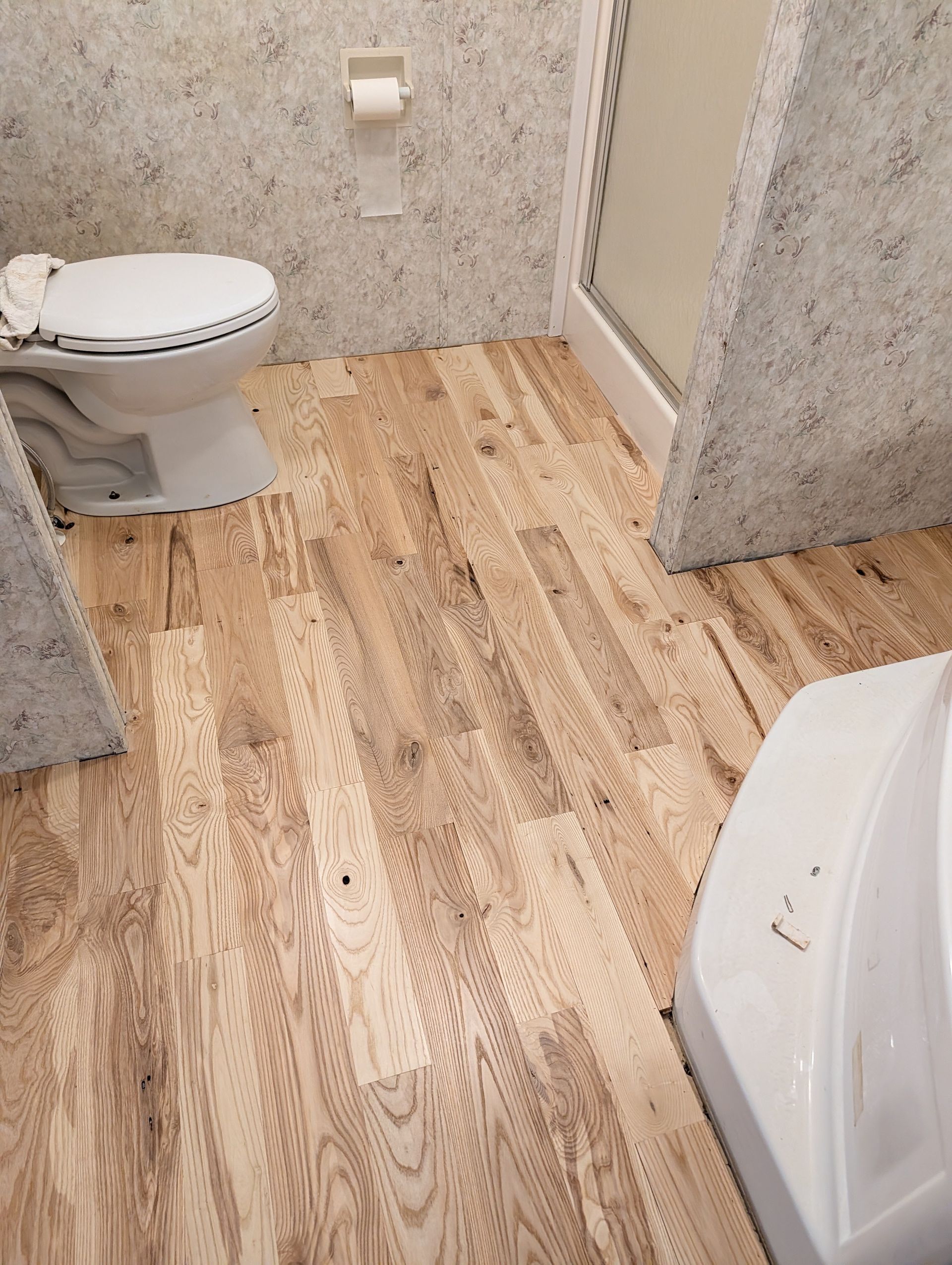 Bathroom with light wood floor, toilet, and shower stall