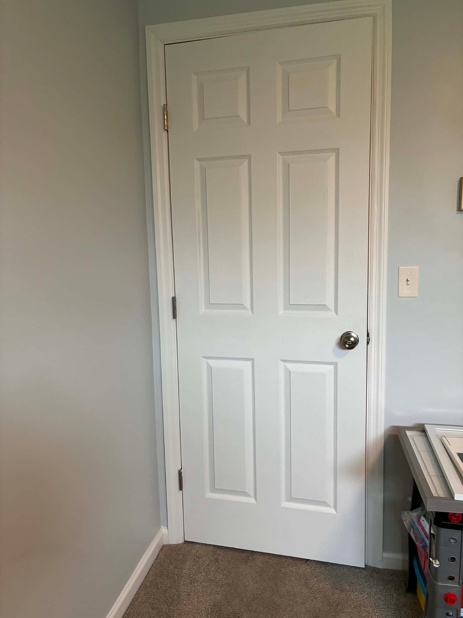 White paneled closet door with silver knob in a light gray room; vacuum and storage bin at right.