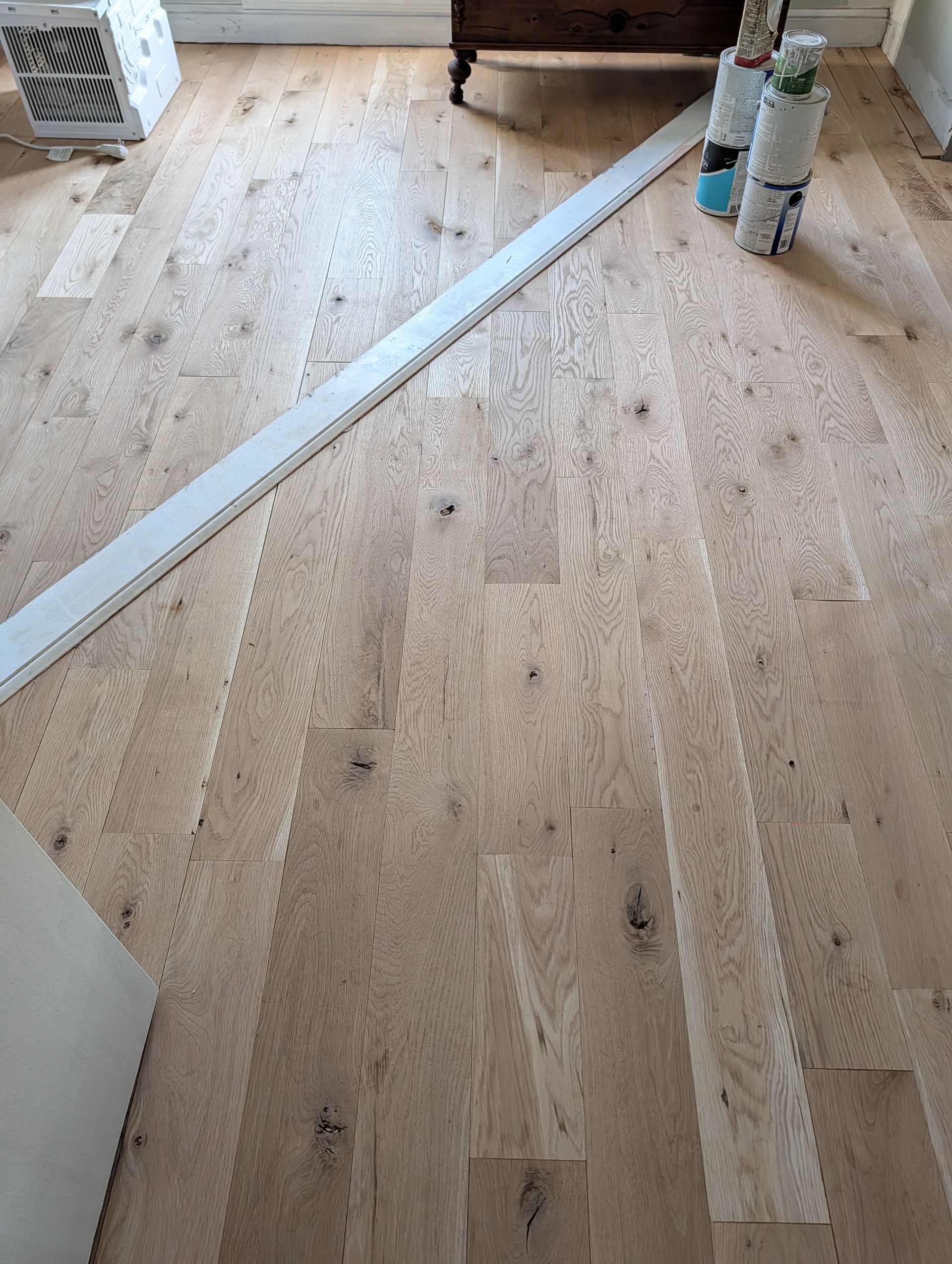 Light wood floor with a long white strip and a radiator in the corner of a room