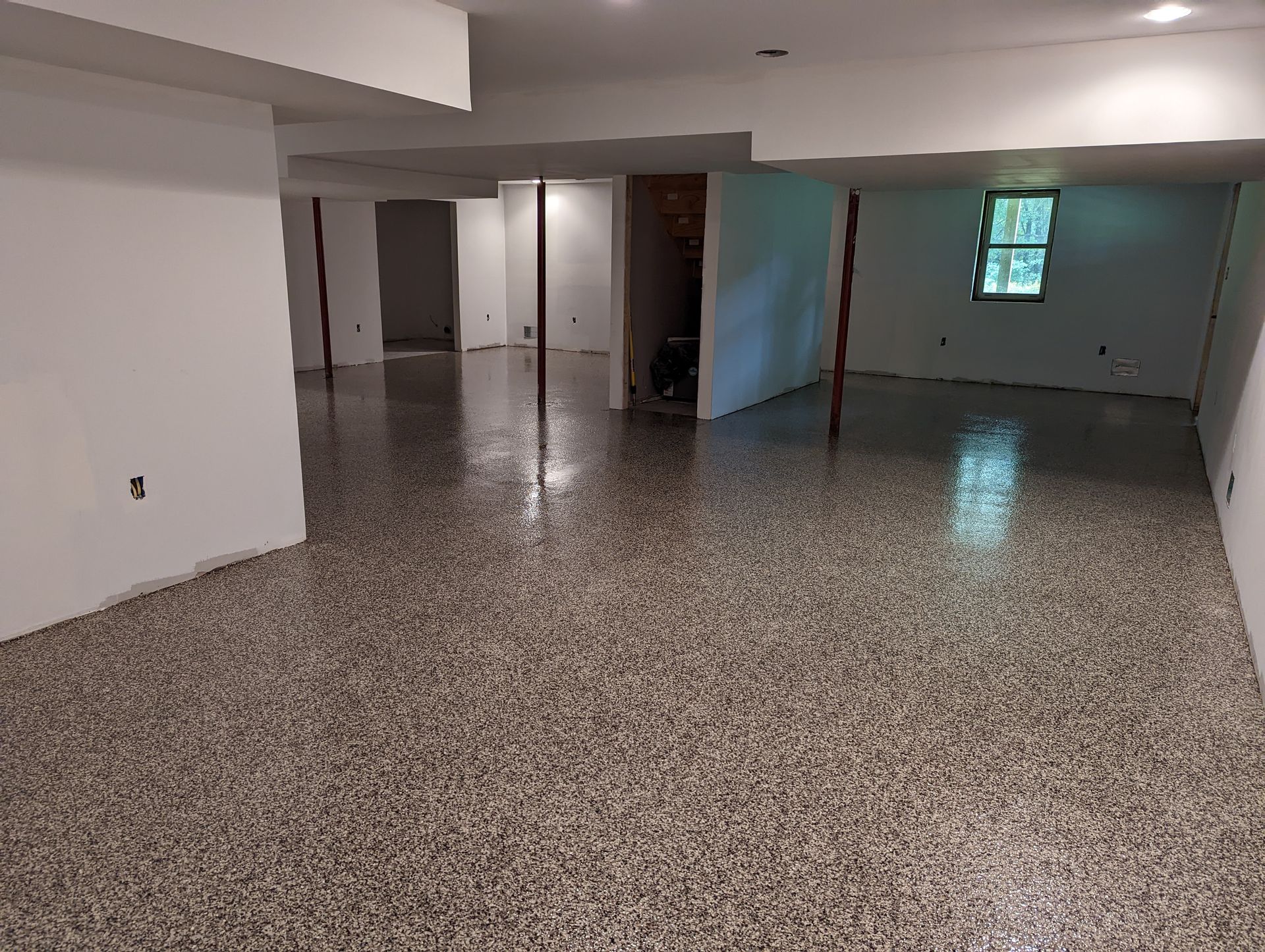 Empty basement with speckled tile floor, white walls, recessed lights, and a small window.