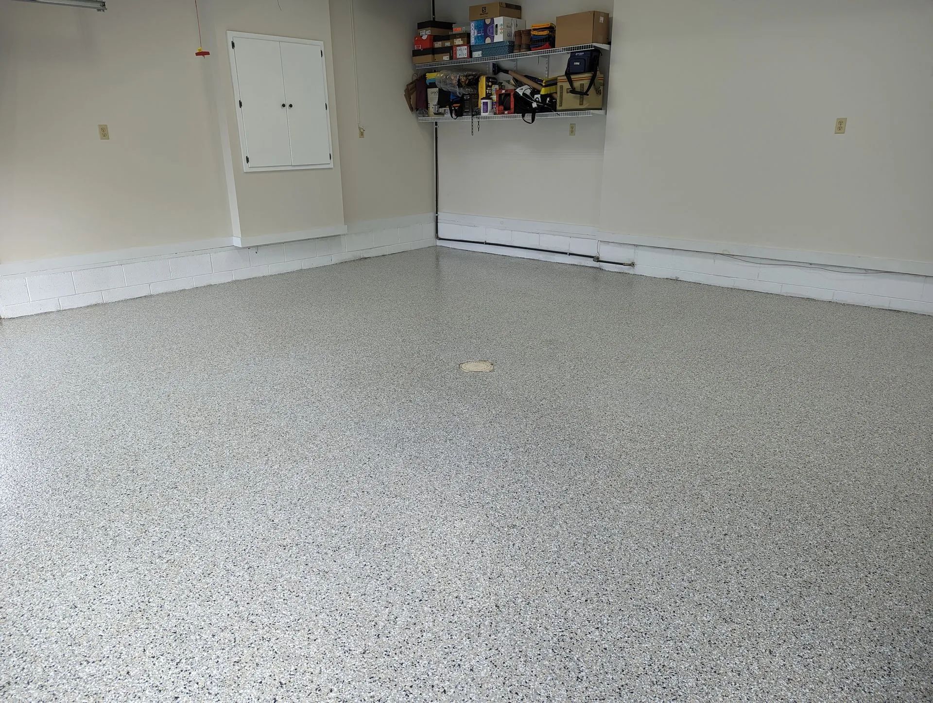 Empty garage with speckled epoxy floor and storage shelves on the back wall