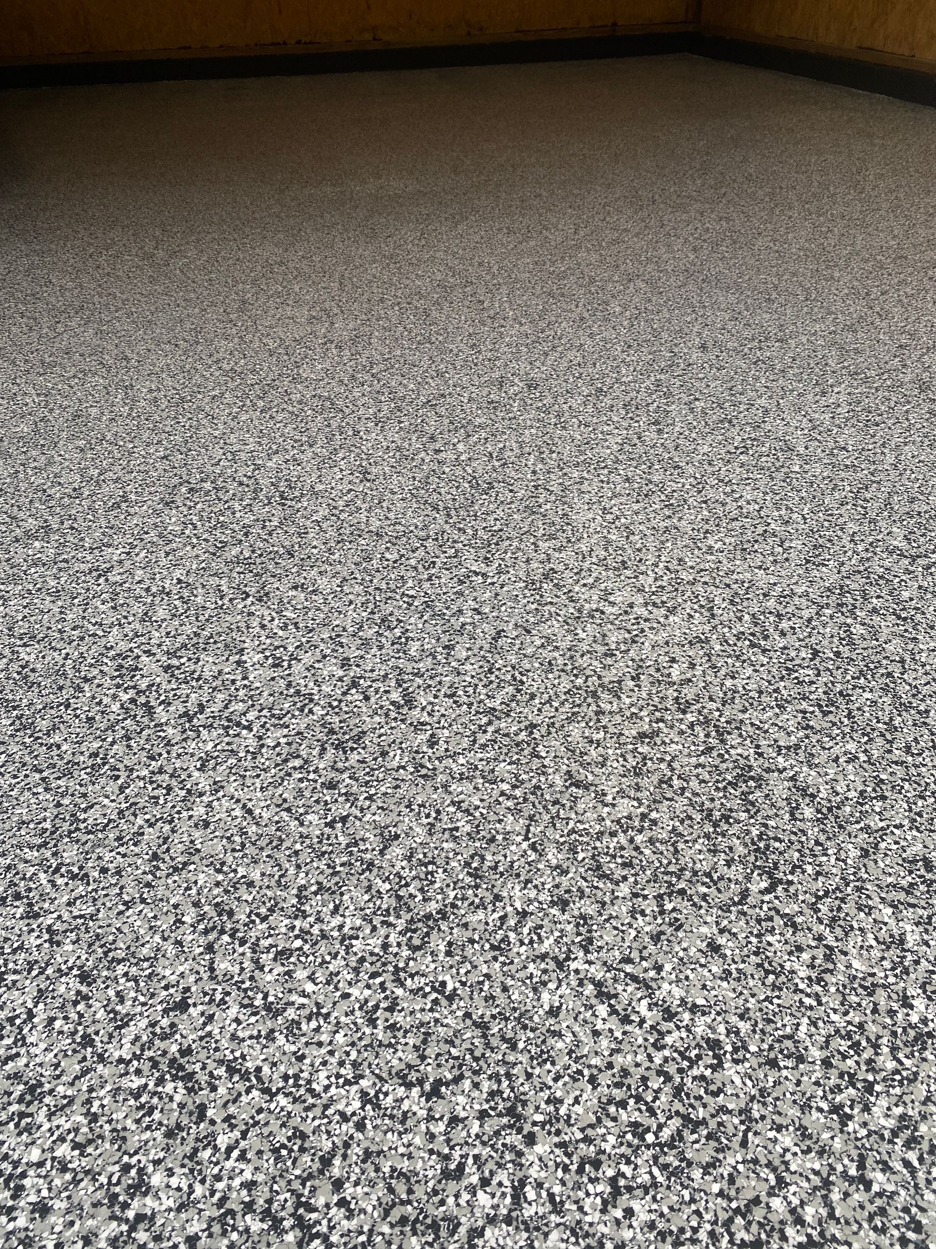 Speckled gray carpet in an indoor room with a dark wall edge at the top.