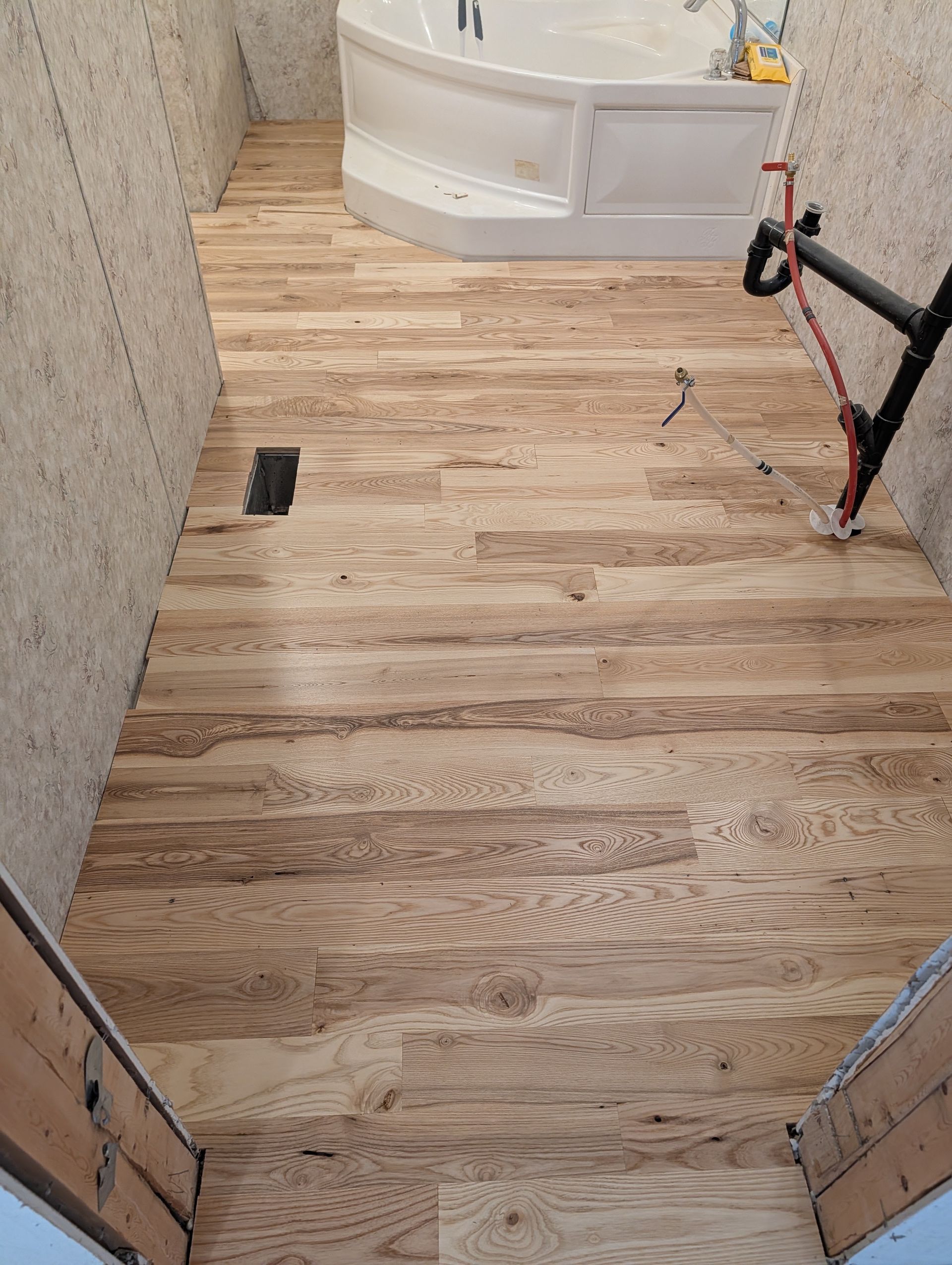 Wooden stair landing under construction with tiled wall, bathtub, and exposed pipes in a bathroom.