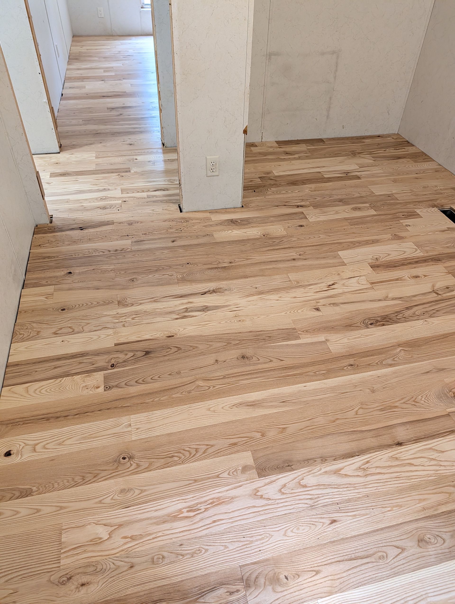 Empty room with newly sanded light wood floor and white walls, showing a doorway and center column.