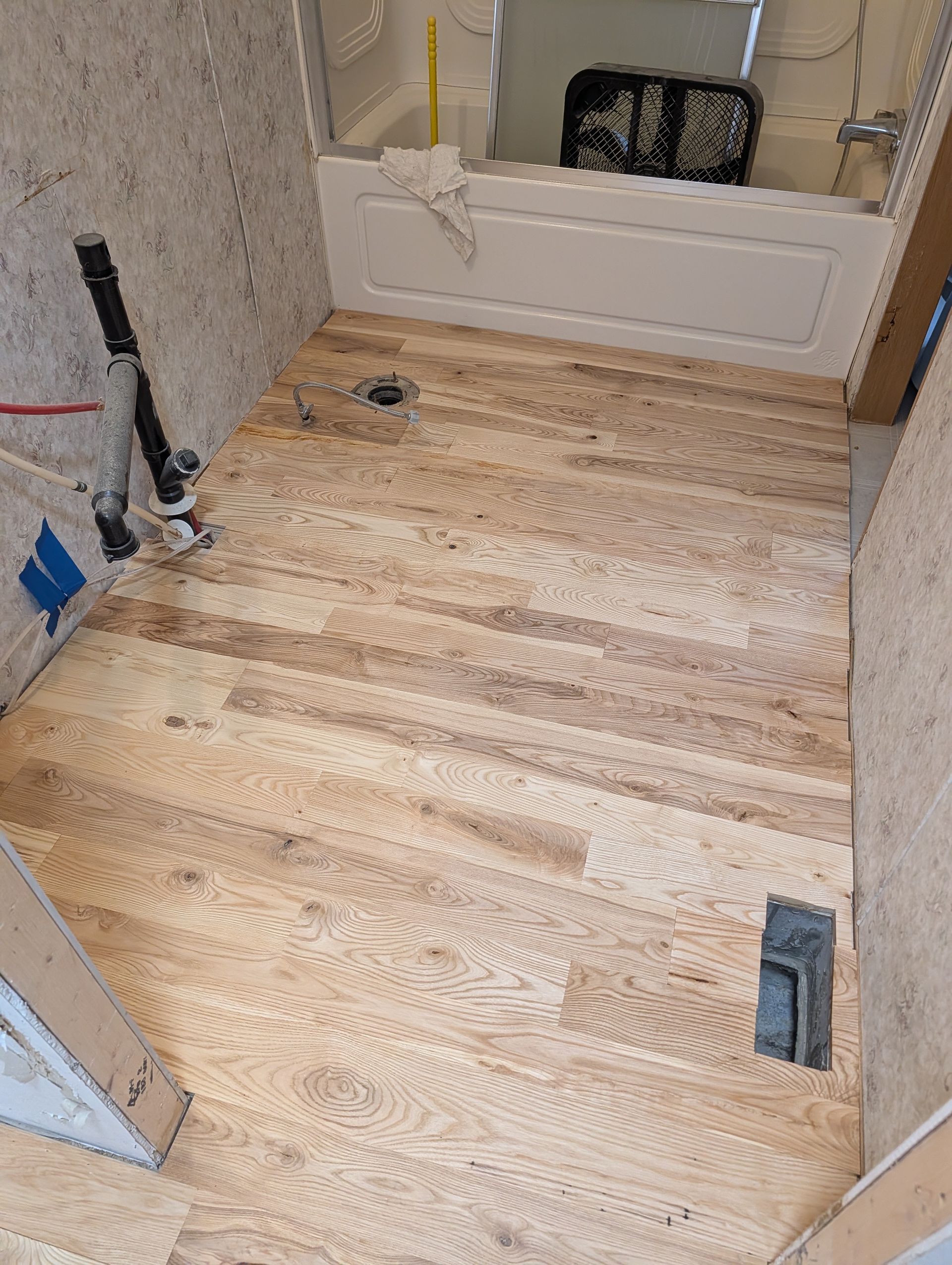 Small bathroom under renovation with unfinished wood subfloor, toilet opening, and tools near the wall.