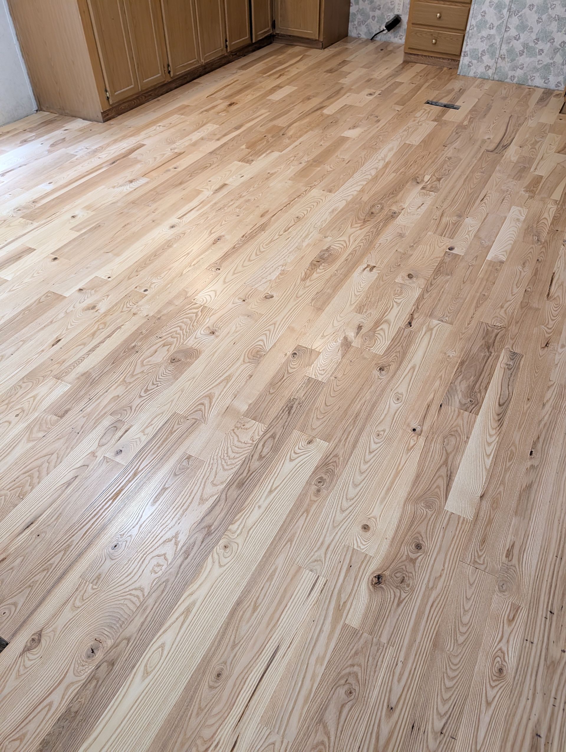 Light wood floor in an empty room with cabinets along the wall
