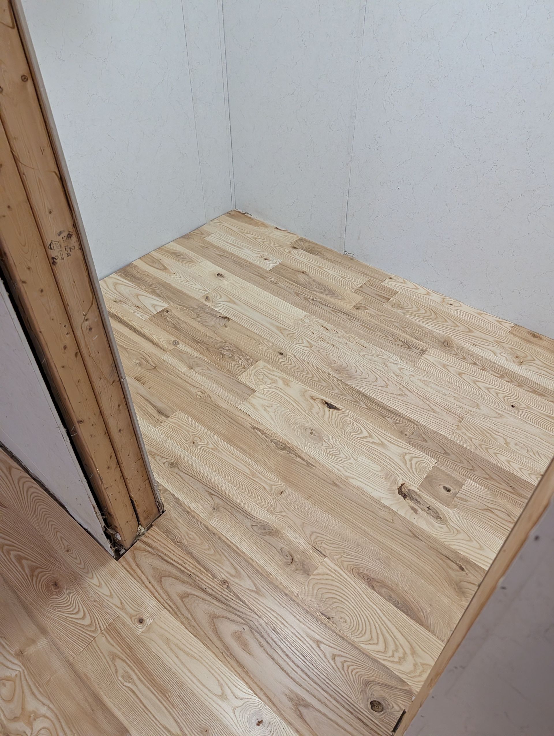Empty light wood floor in a small corner room with unfinished walls and a doorway trim