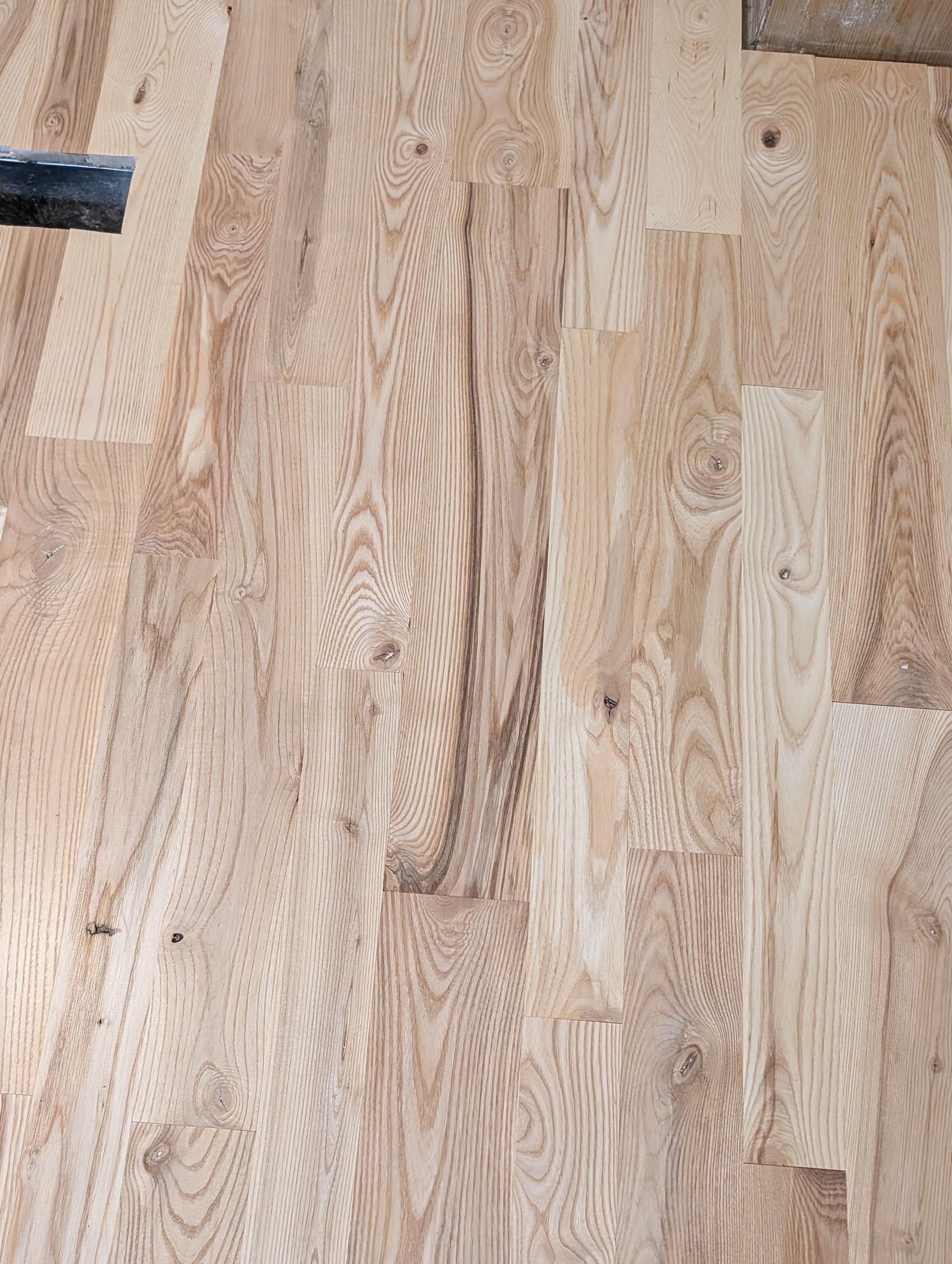 Light wood plank floor with visible grain patterns and a dark object at the upper left edge
